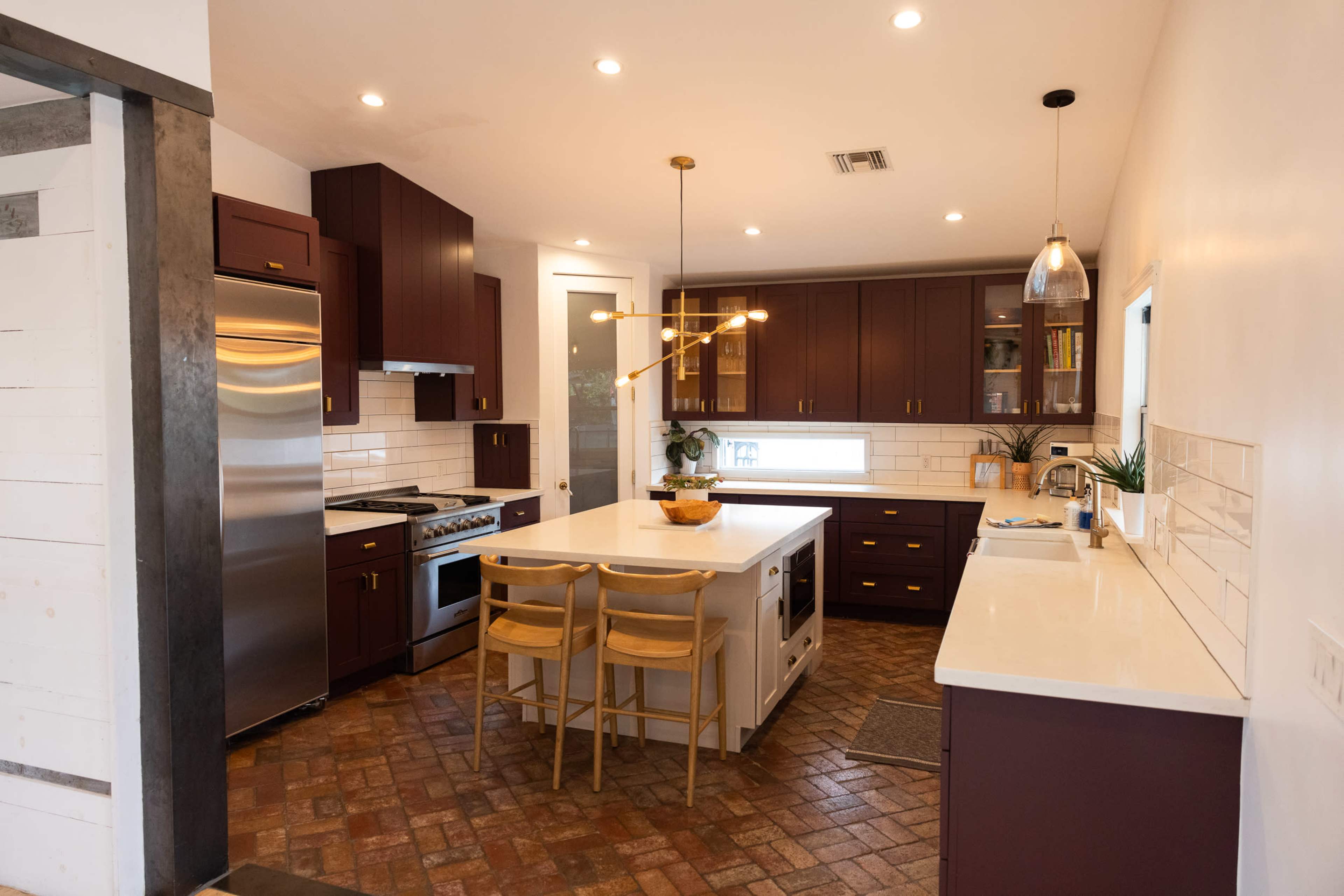 A modern kitchen features dark cabinetry, stainless steel appliances, a central island with seating, and ample countertop space illuminated by overhead lighting.