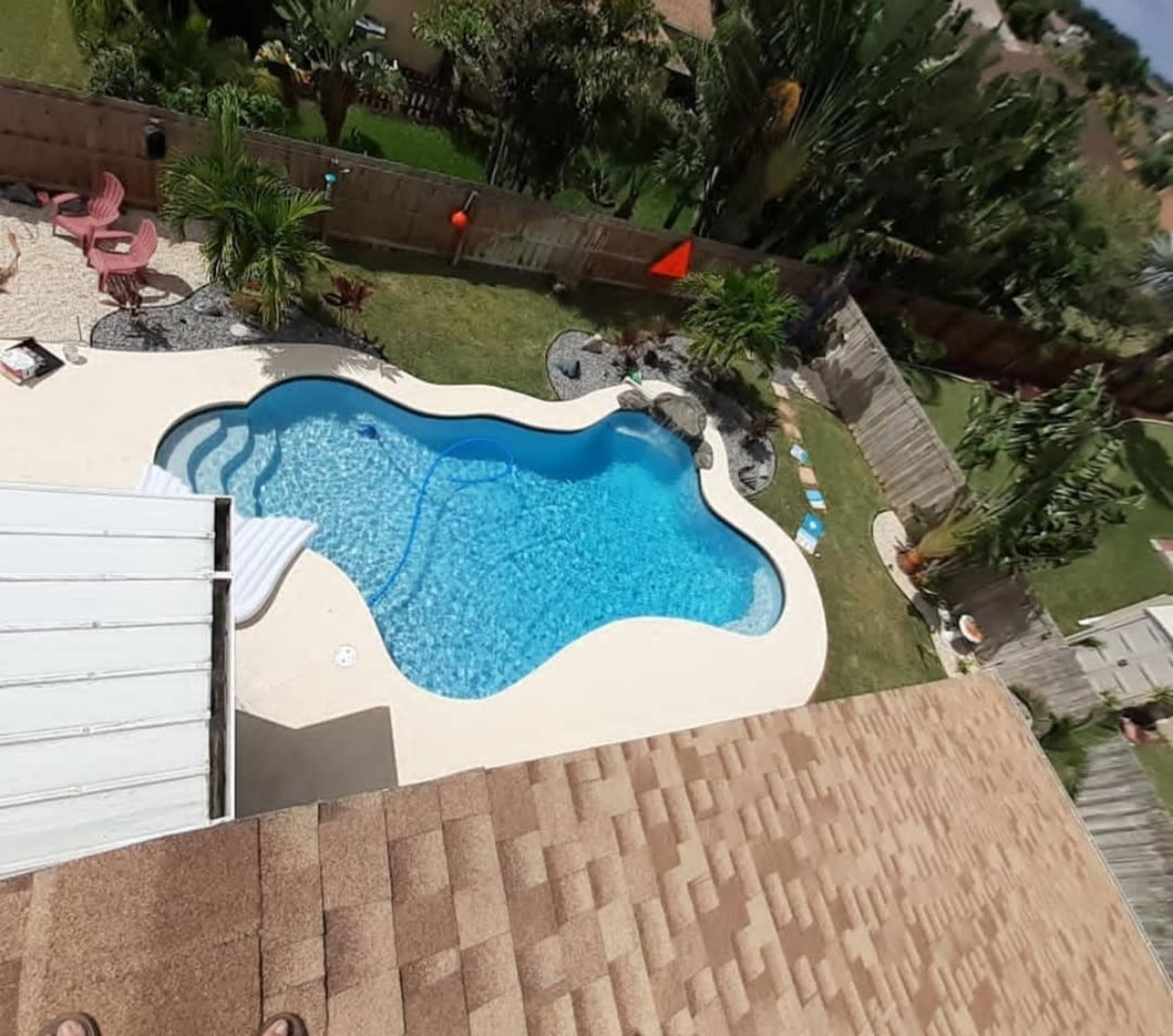 The image shows an aerial view of a backyard with a swimming pool, surrounded by landscaping and lounge chairs.