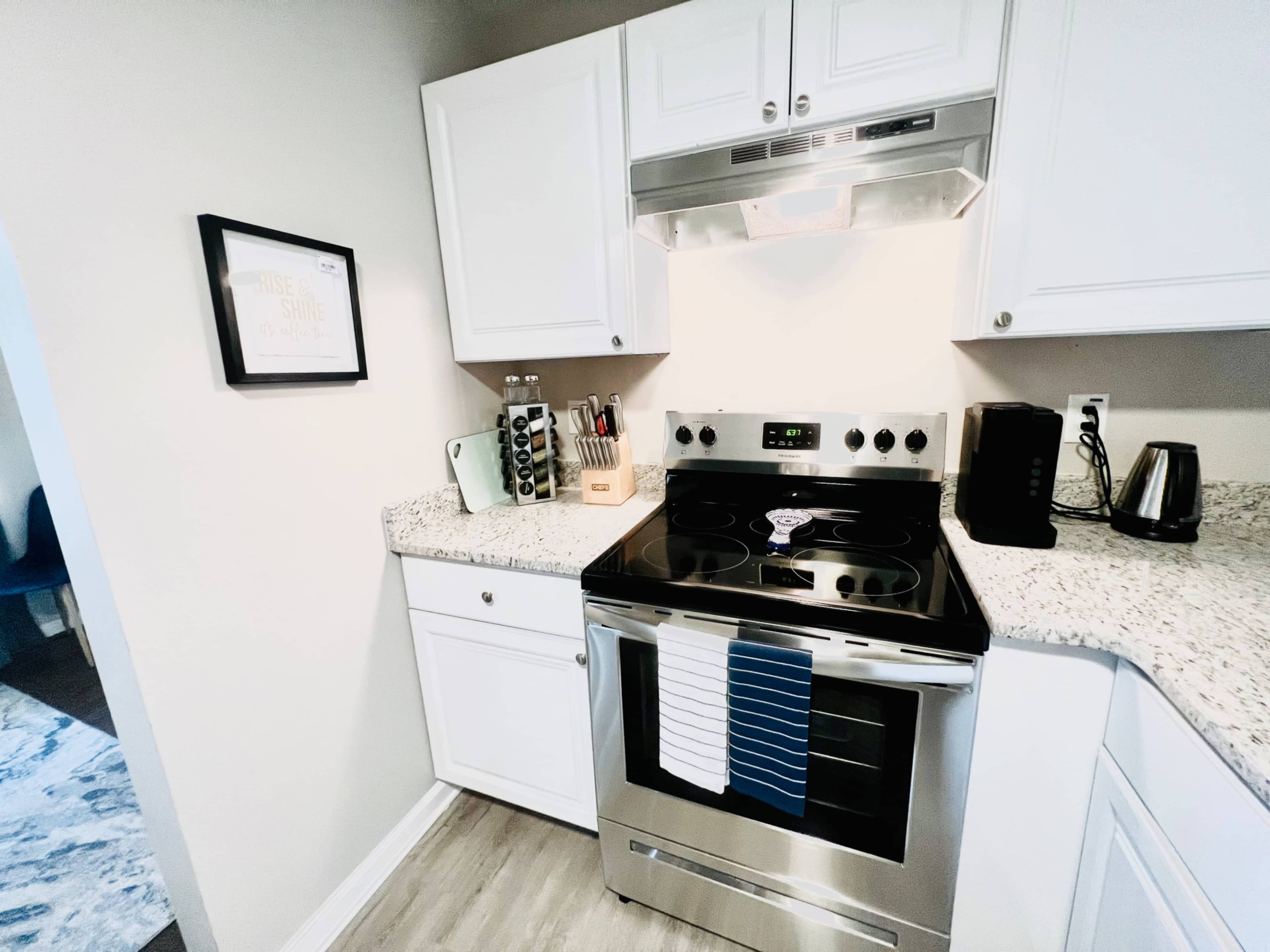 A compact kitchen features white cabinetry, a stainless steel oven, and a granite countertop with kitchen appliances.