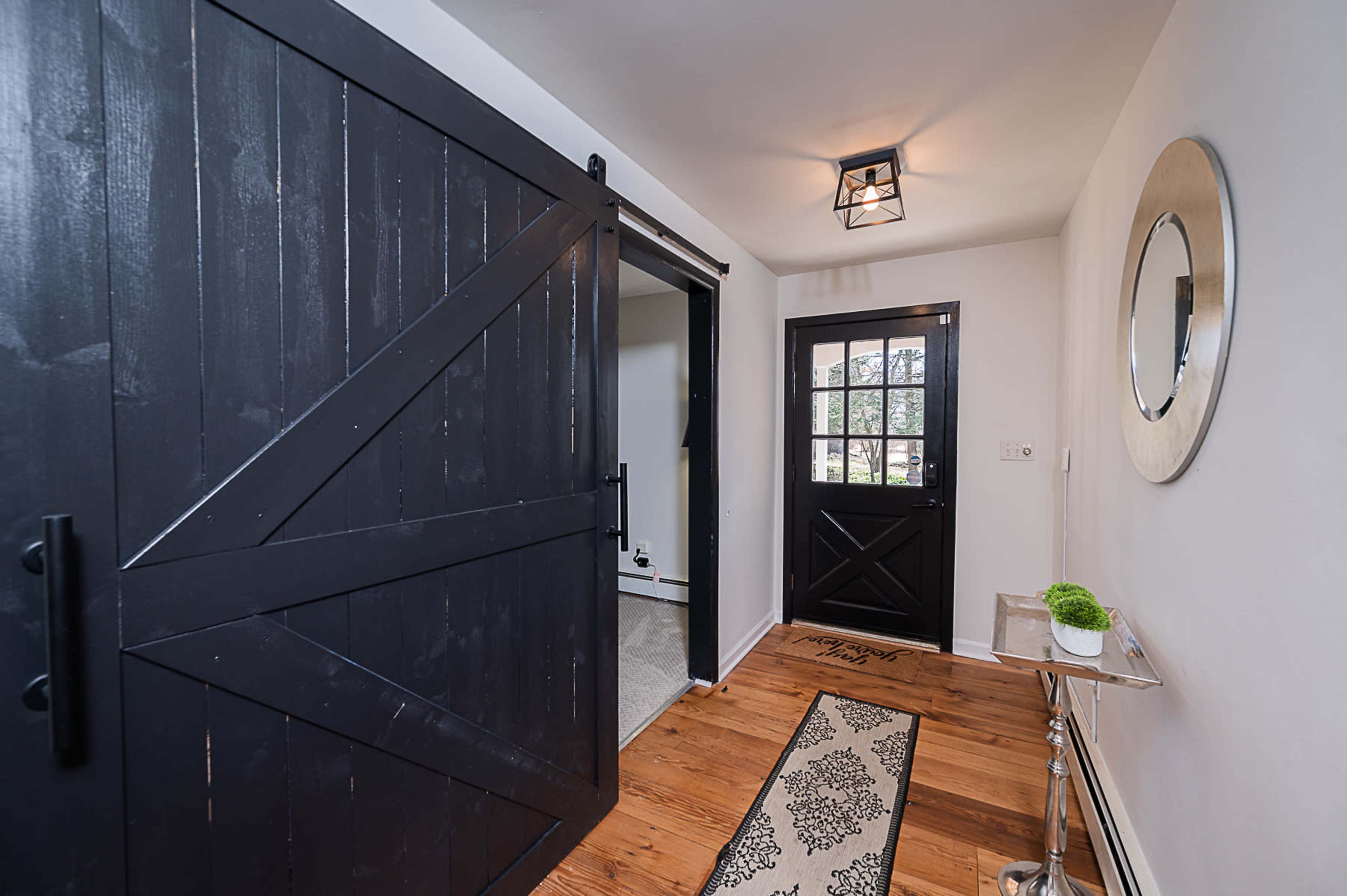 The entryway features a wooden barn-style door and a black front door, complemented by a round mirror and a patterned rug on a hardwood floor.