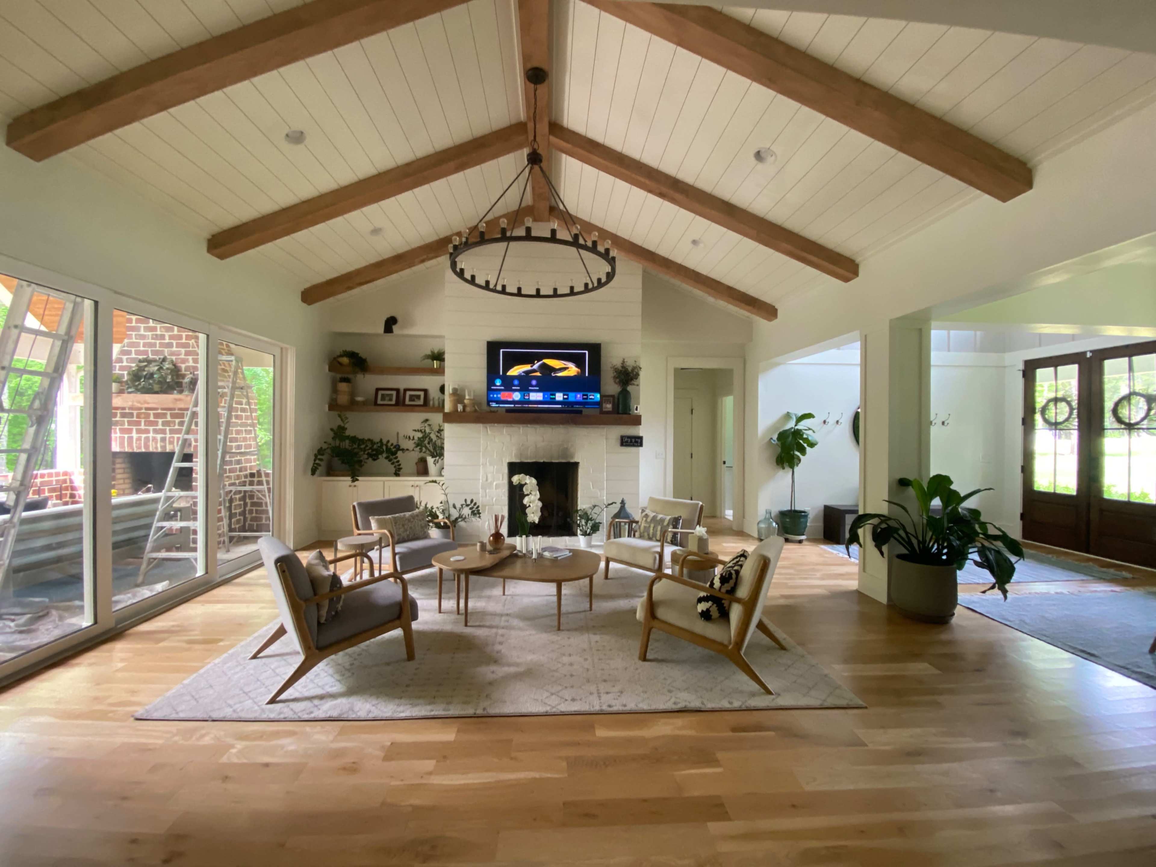 A spacious living room with a vaulted ceiling, wooden beams, a light-colored fireplace, and a seating arrangement centered around a coffee table.