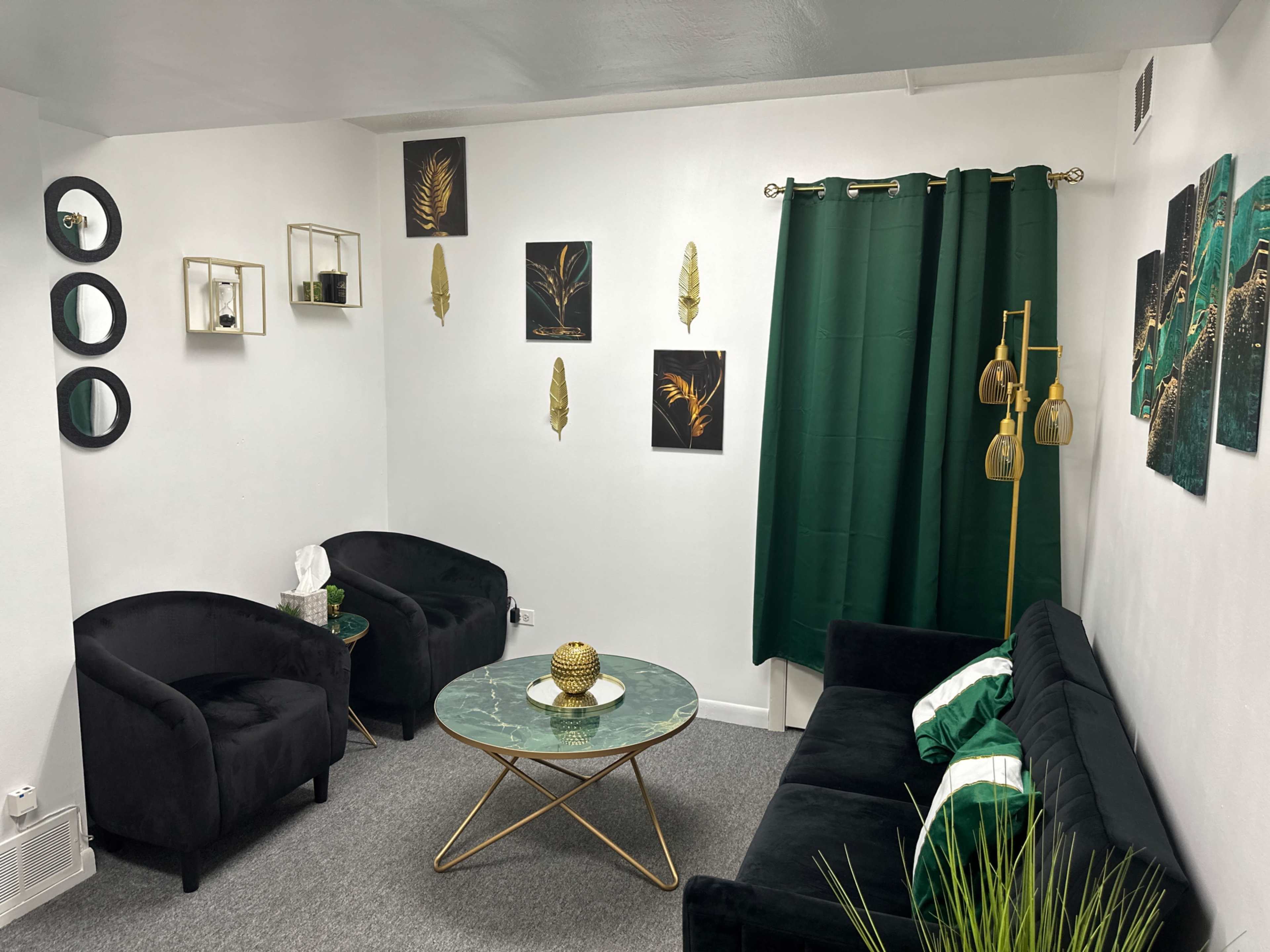A living room with a green and black color scheme, featuring two black chairs, a green sofa, a circular coffee table, and decorative wall art.