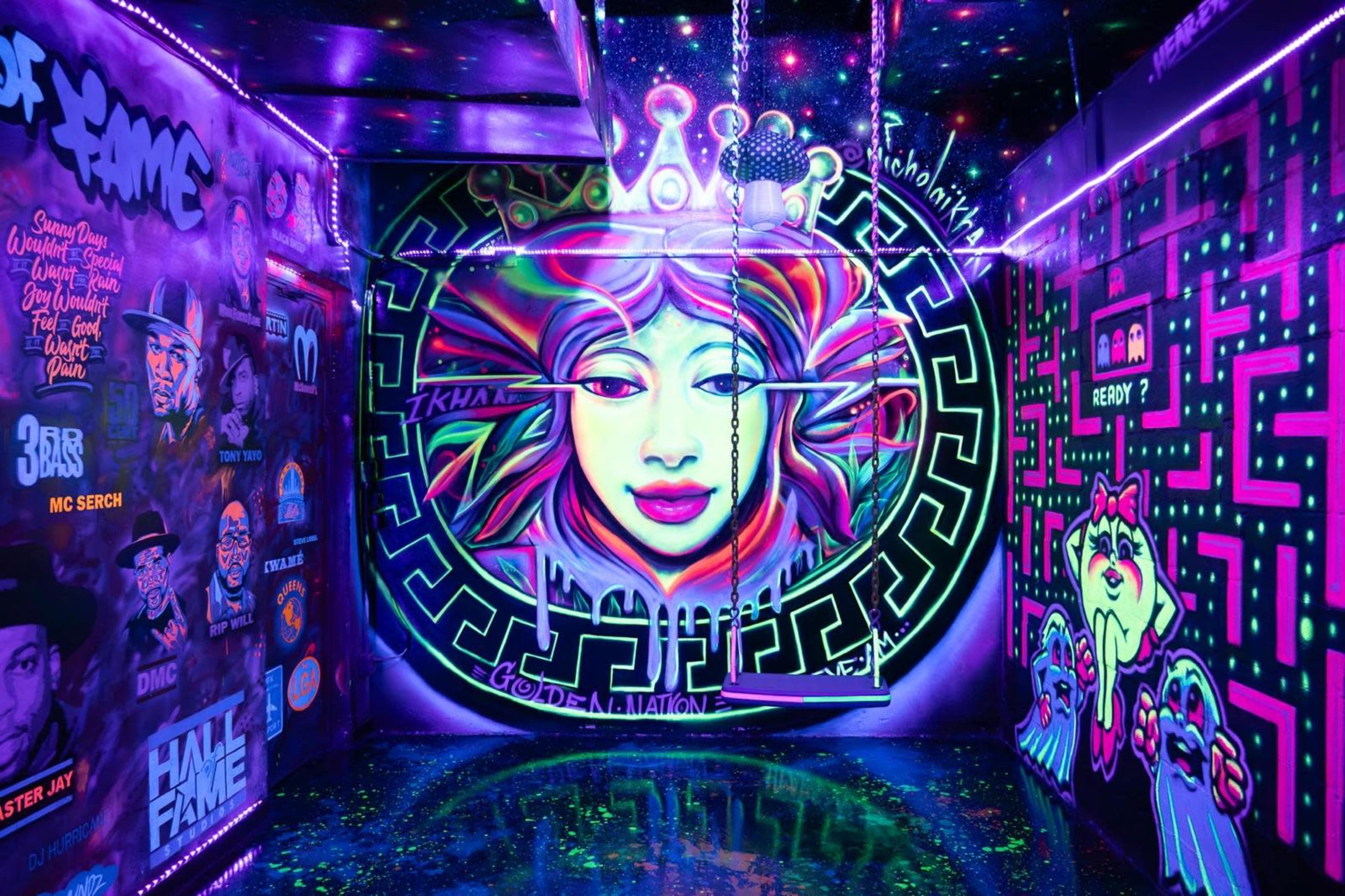 A vibrant, neon-colored graffiti mural of a woman's face on a wall within a small, illuminated room adorned with various other colorful designs.