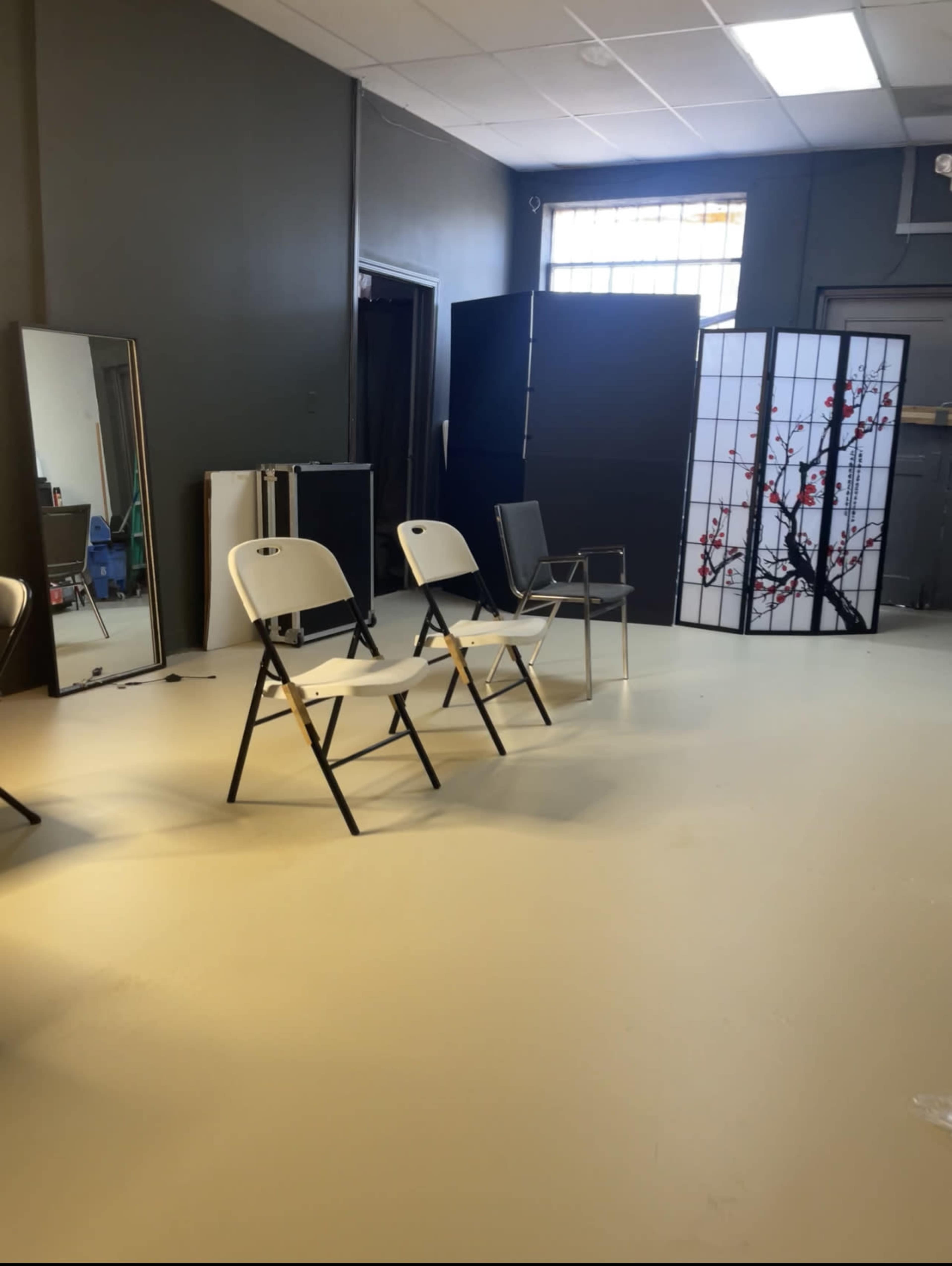A room with several folding chairs arranged on a light-colored floor, flanked by mirrors and a decorative room divider in the background.