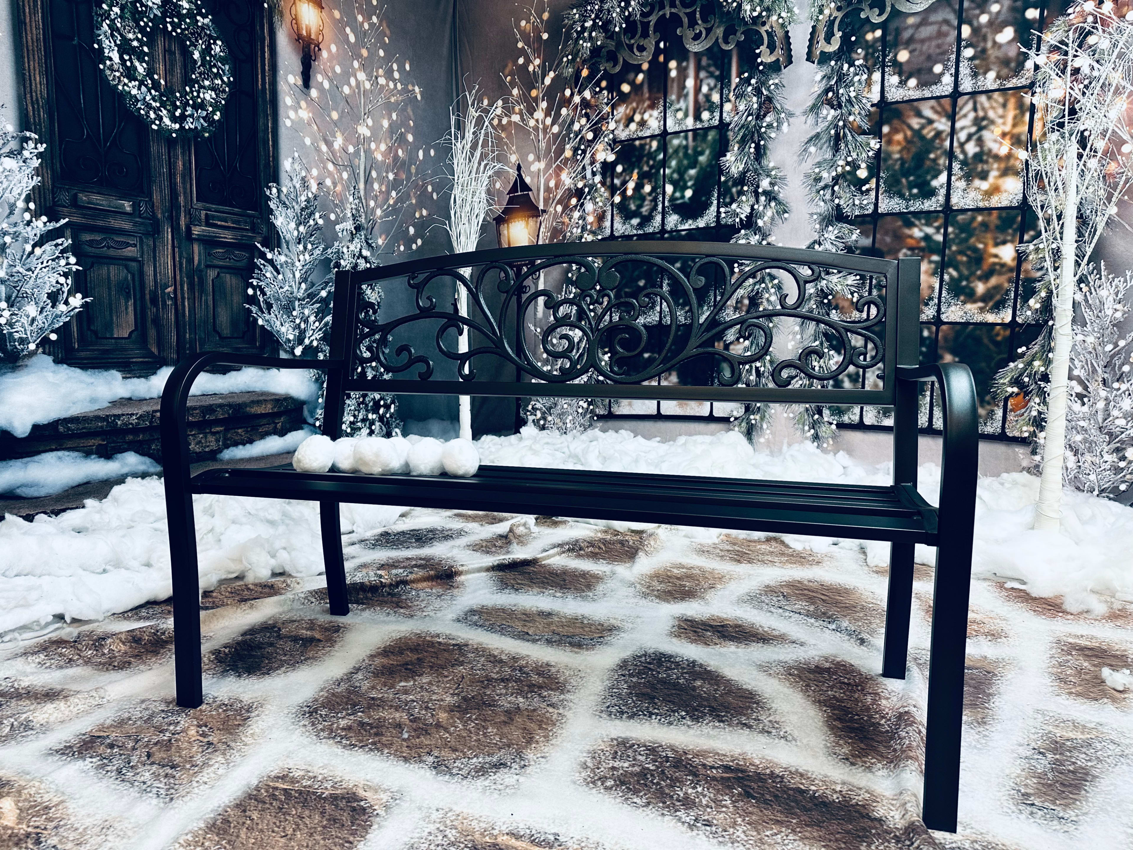A black ornate bench sits on a snowy pathway surrounded by twinkling lights and frosty trees.