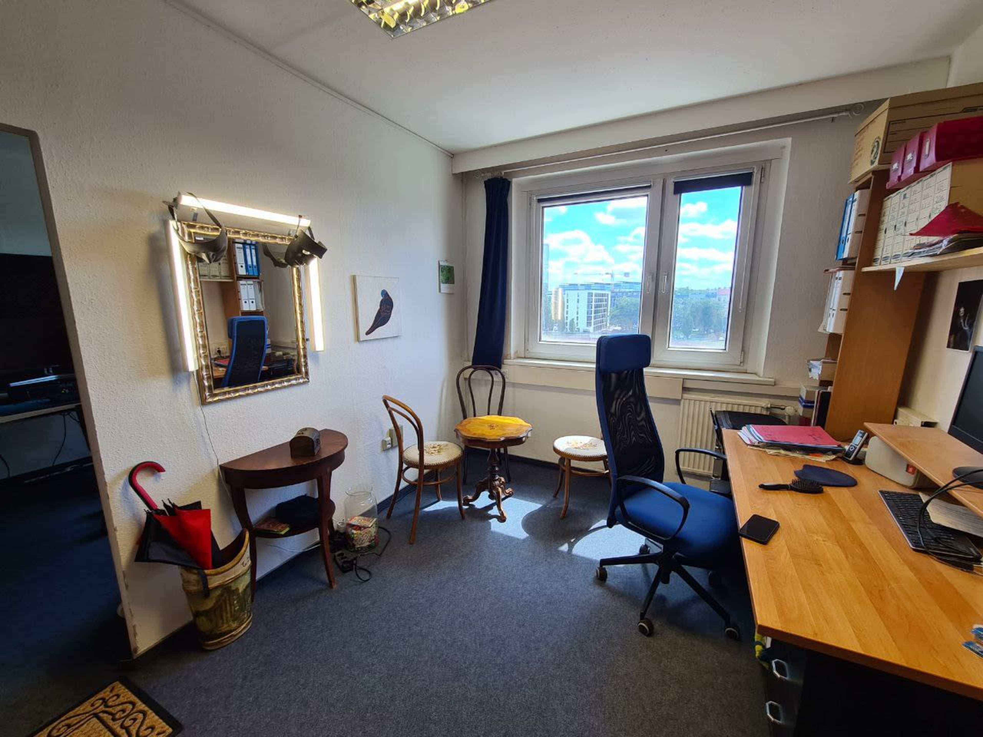 The image shows a sparsely furnished office with a desk, a chair, a small round table, and a decorative mirror on the wall.