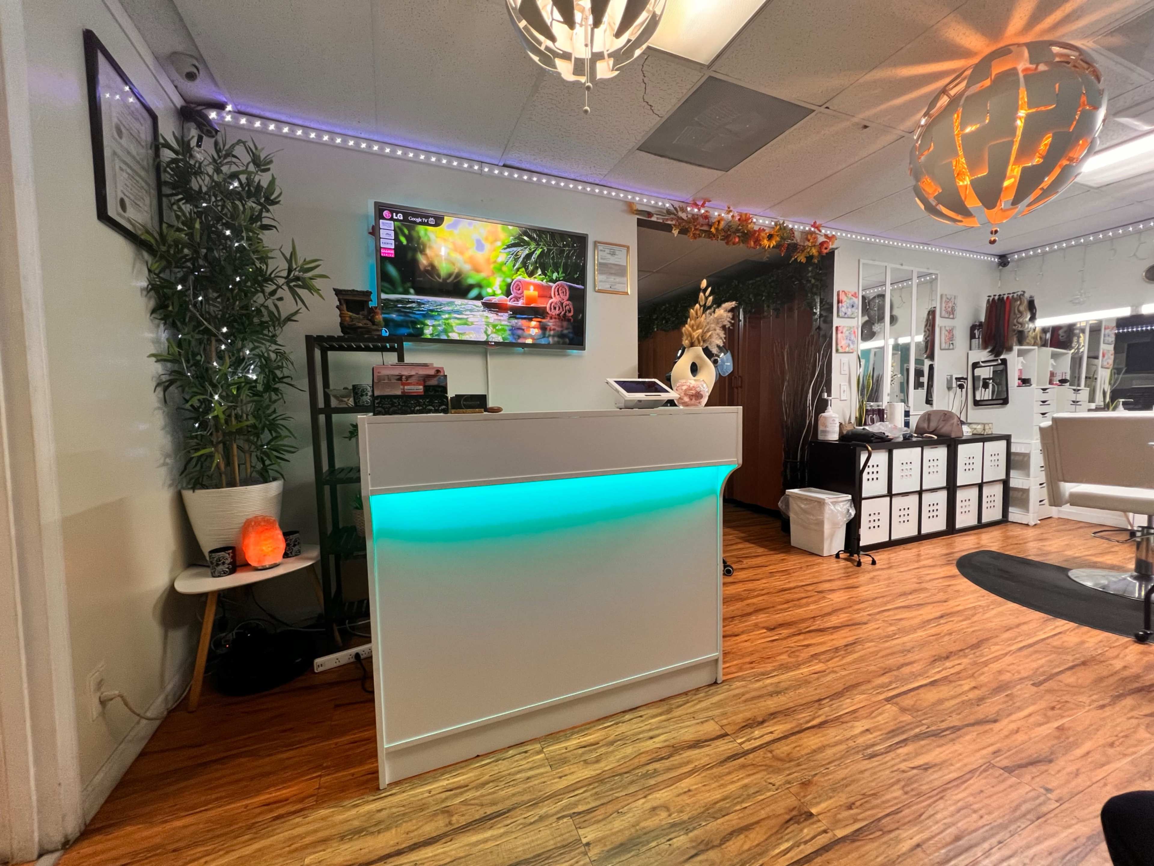 The image shows a modern reception area with a sleek, illuminated front desk, a television displaying colorful graphics, and various decorative elements including plants and lighting fixtures.