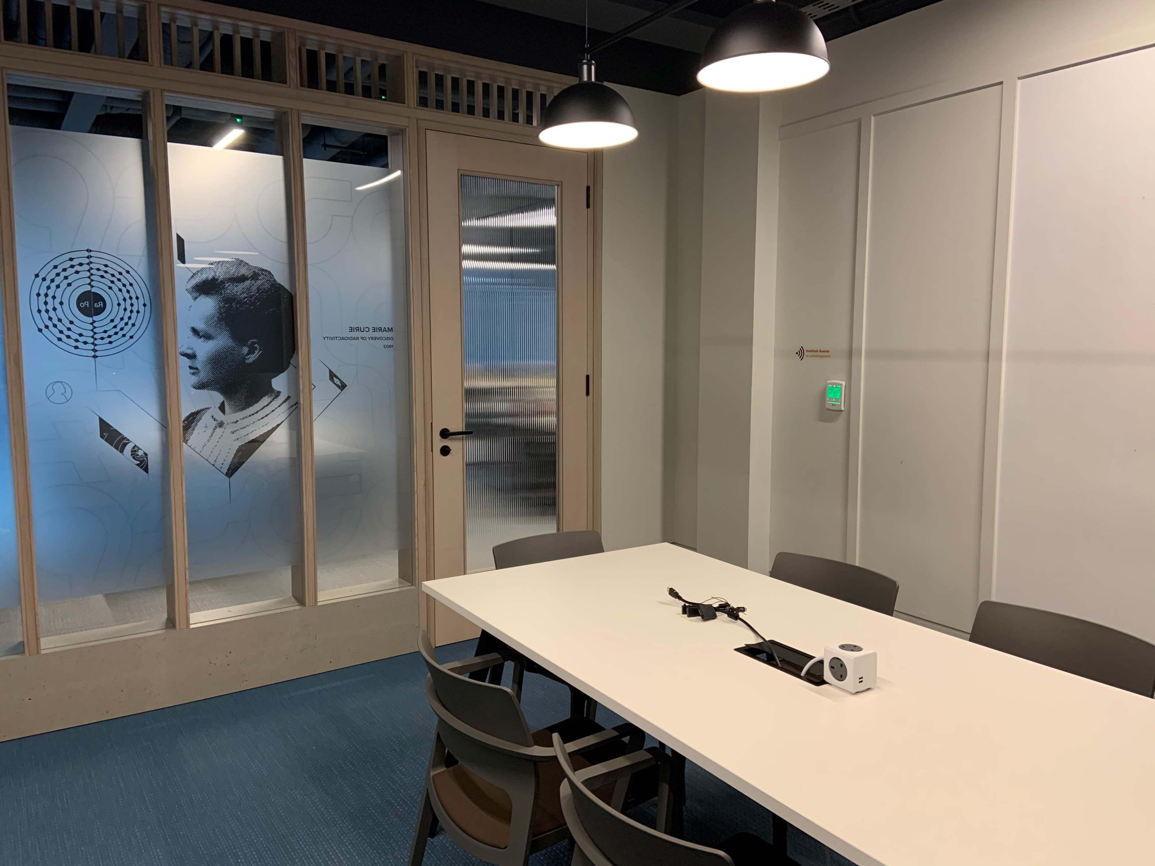 The image shows a modern meeting room with a white table and several chairs, featuring a large wall graphic of a profile in the background.