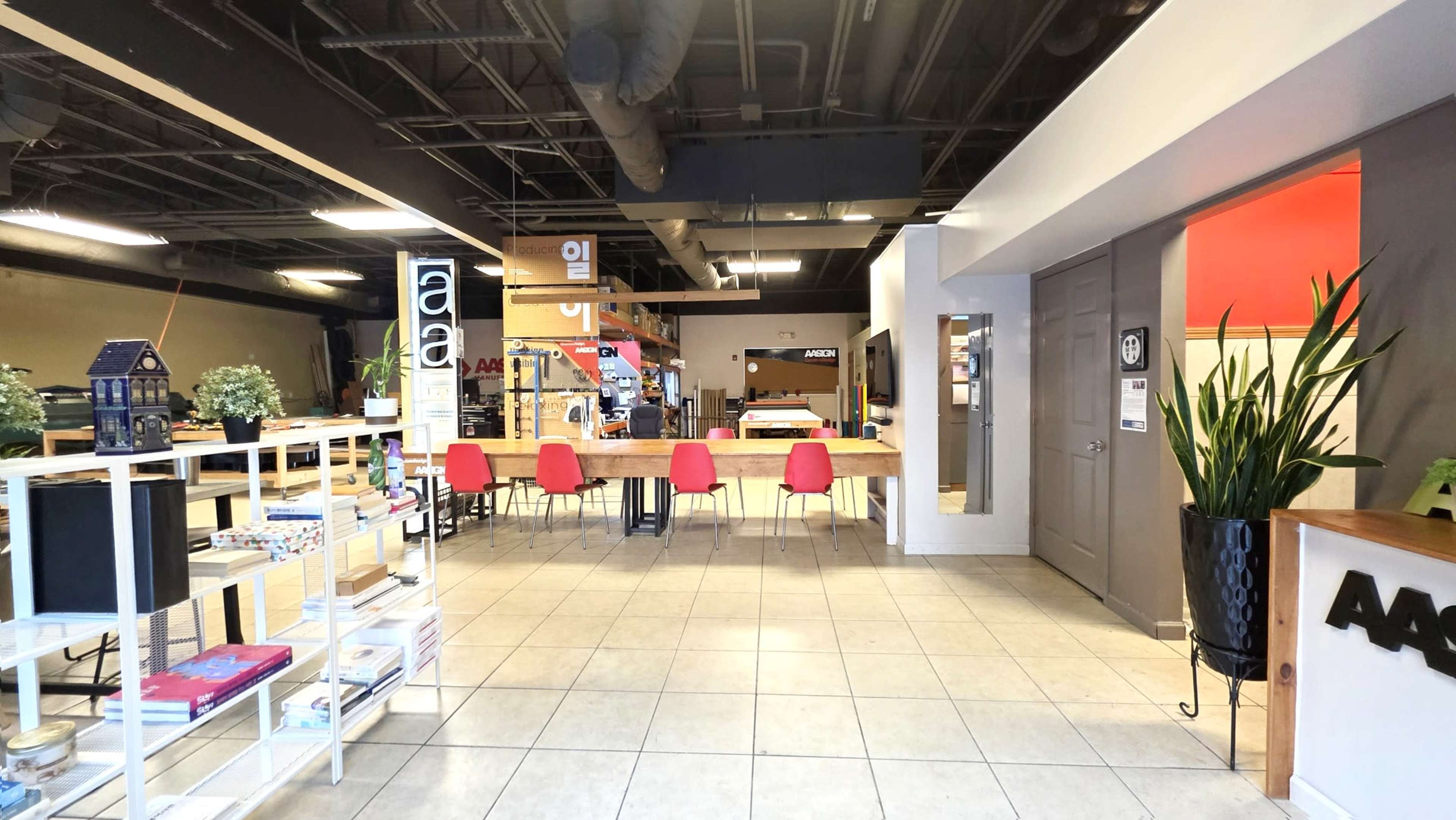 The image shows an interior space with a reception area featuring a long wooden counter, red chairs, and various shelves displaying items.