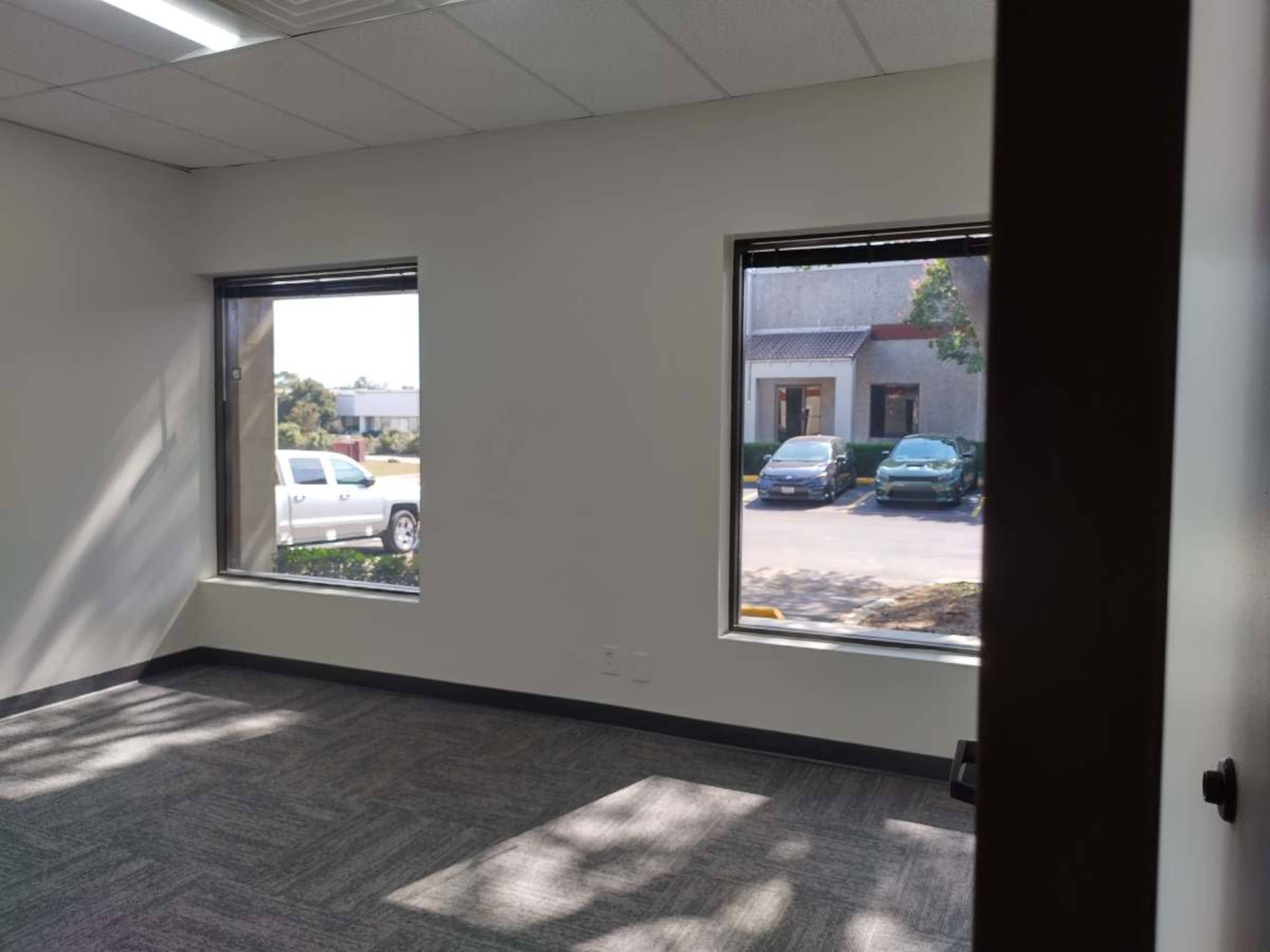 The image shows an empty office space with two windows overlooking parked cars outside.