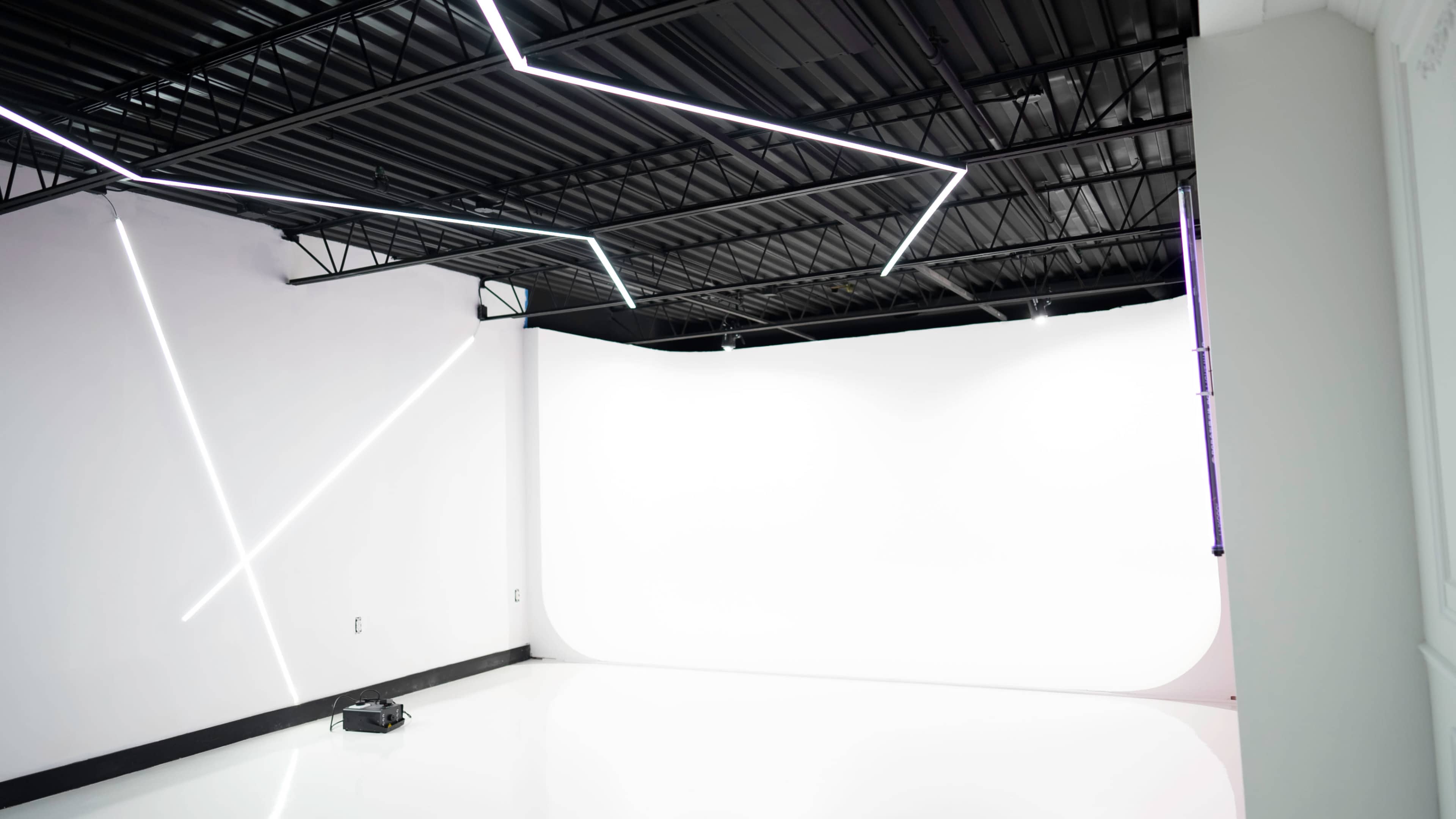 A contemporary photography studio with angular LED lights on the black ceiling and a white backdrop.