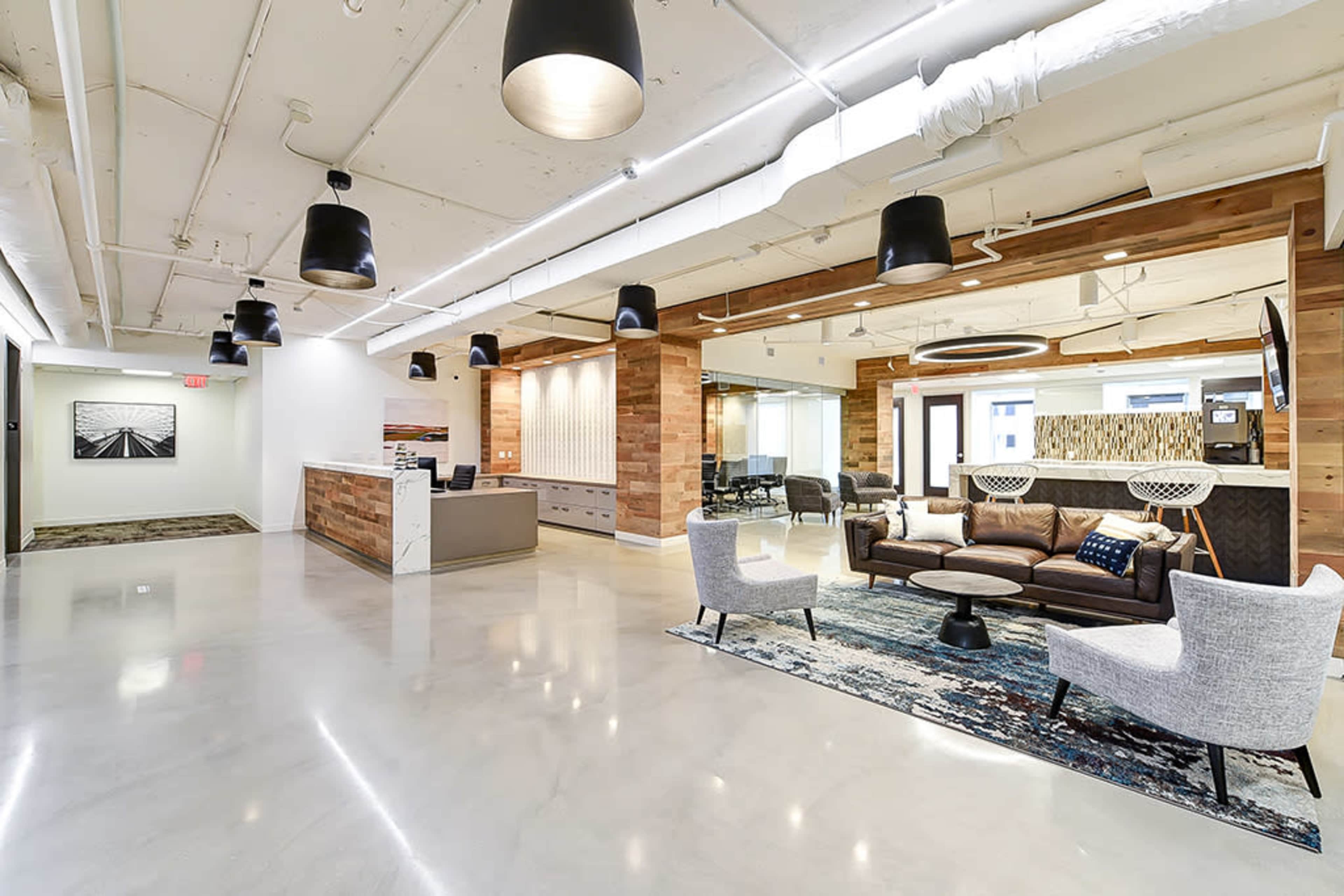 A modern office lobby featuring a reception area, a seating arrangement with a couch and chairs, and wood-paneled walls.