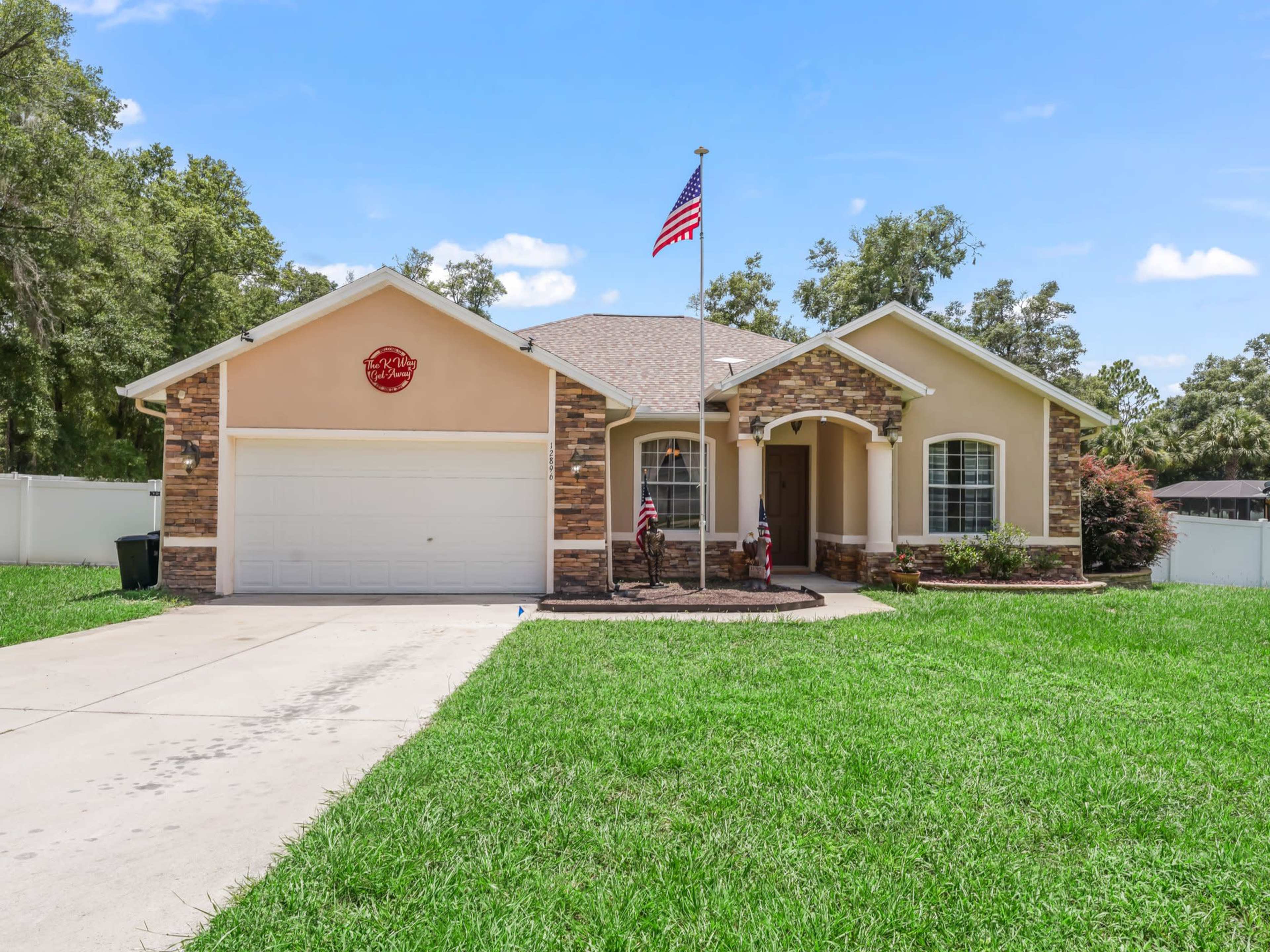 A single-story home features a stone accent facade, a front porch, an American flag, and a neatly manicured lawn.