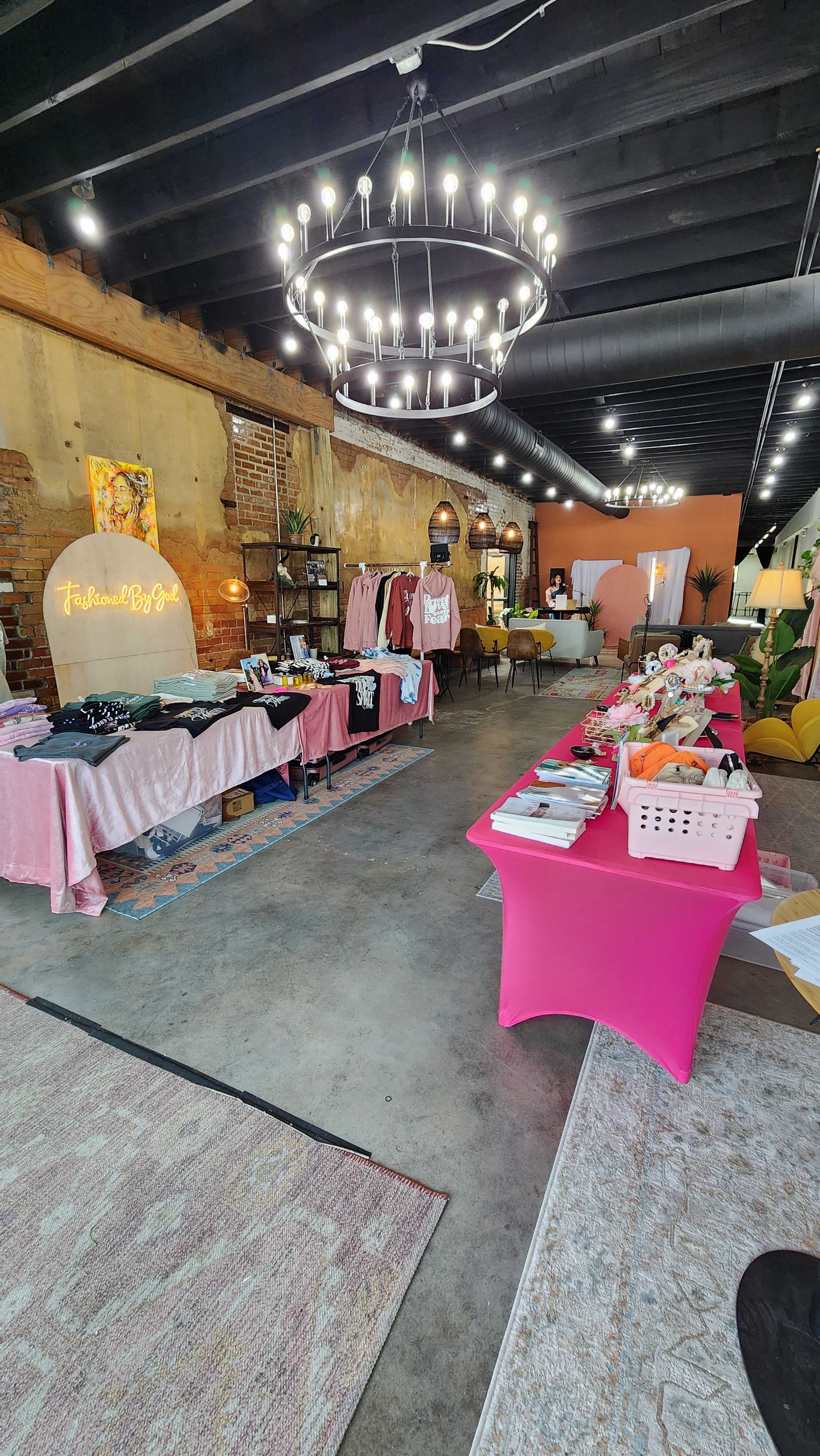 The image shows a boutique interior with clothing displays, decorative lighting, and a mix of pink and neutral furnishings.