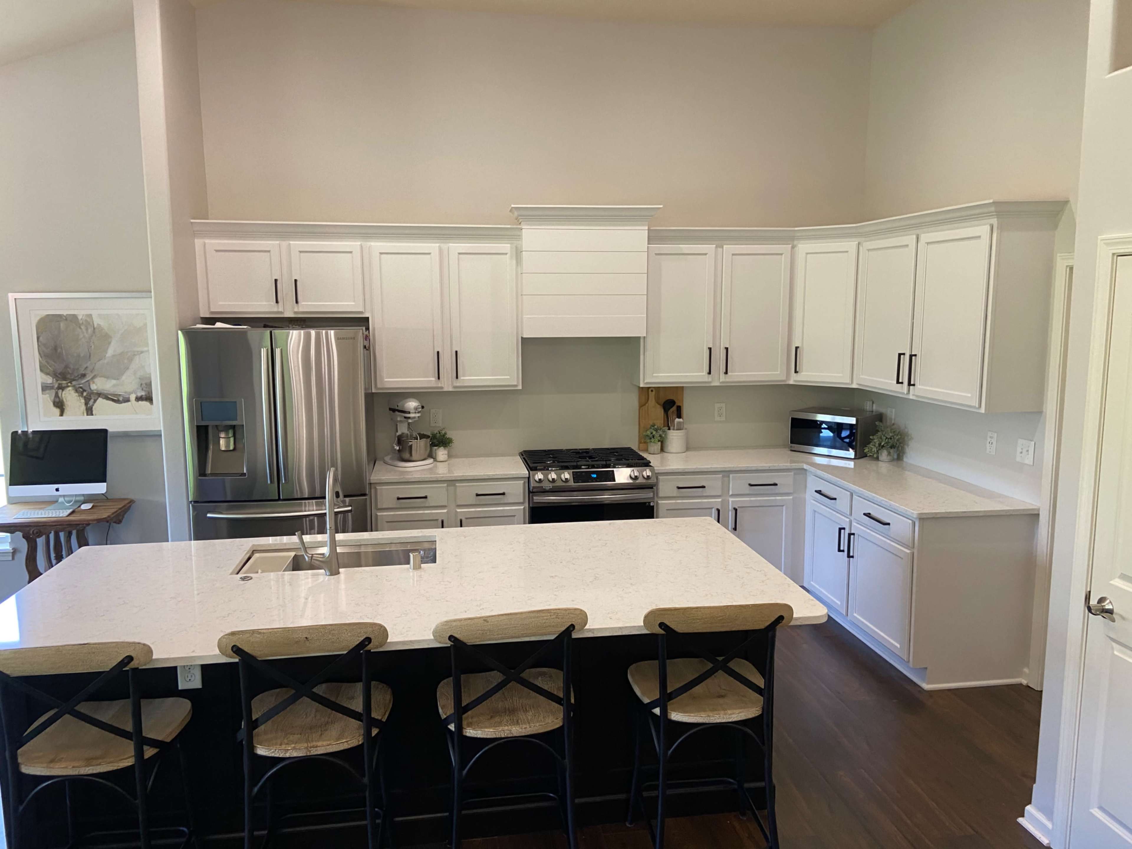 A modern kitchen features white cabinets, stainless steel appliances, a large island with bar stools, and a neutral color scheme.