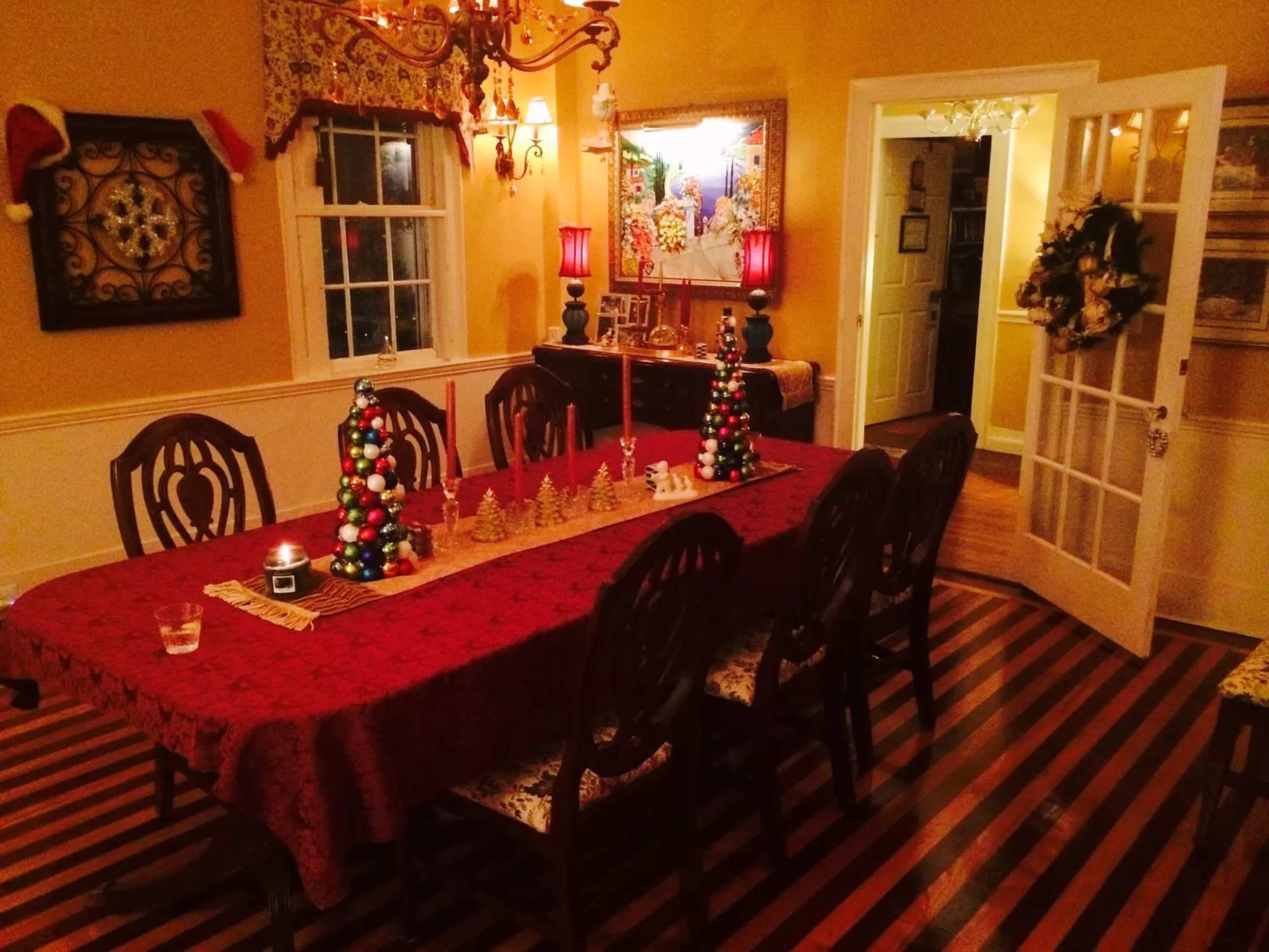 A dining room is set with a red tablecloth, decorative Christmas trees made of ornaments, and a mirrored wall reflecting festive decor.