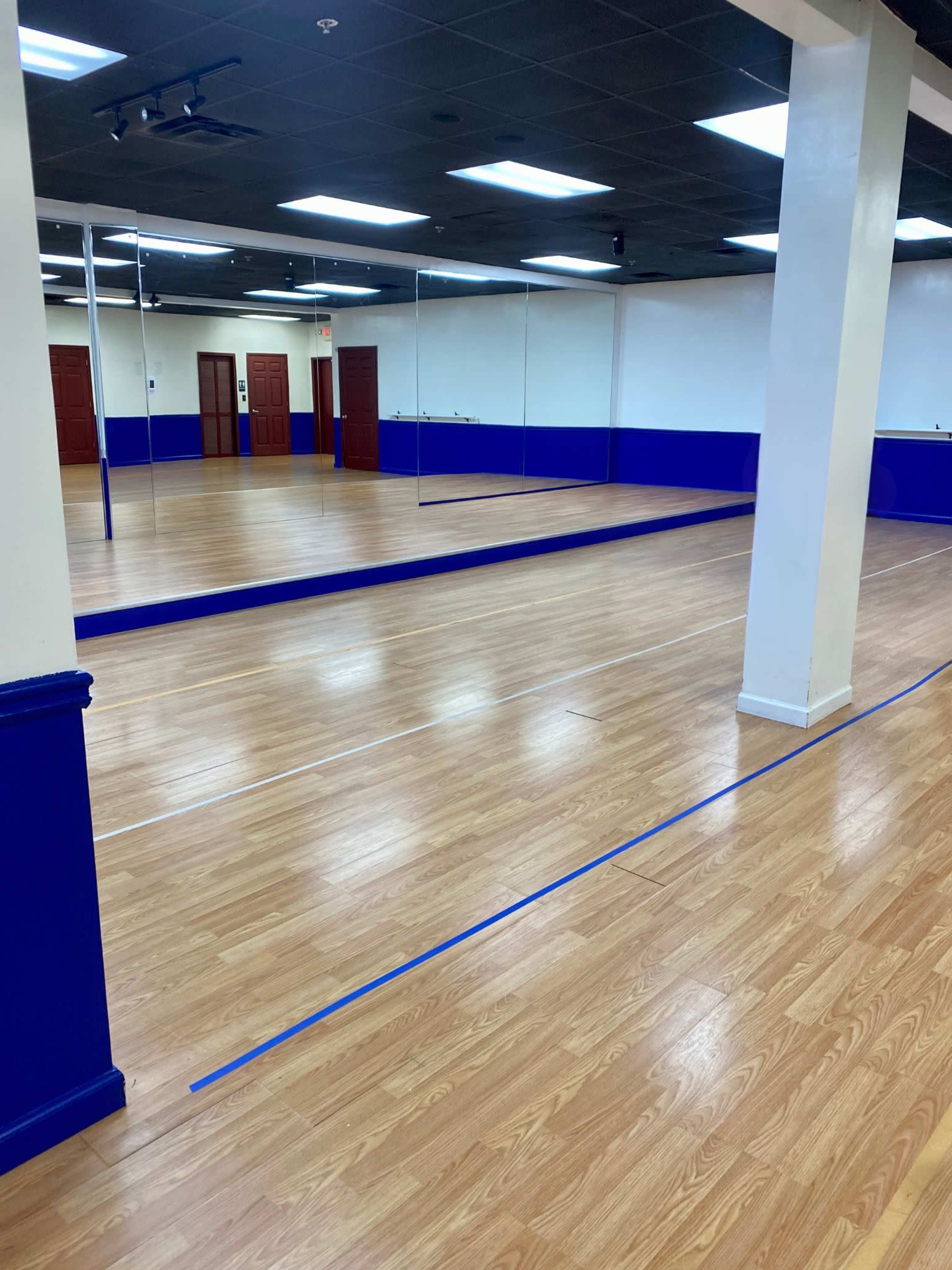 A spacious dance studio with a polished wooden floor, blue wall accents, and mirrored walls.