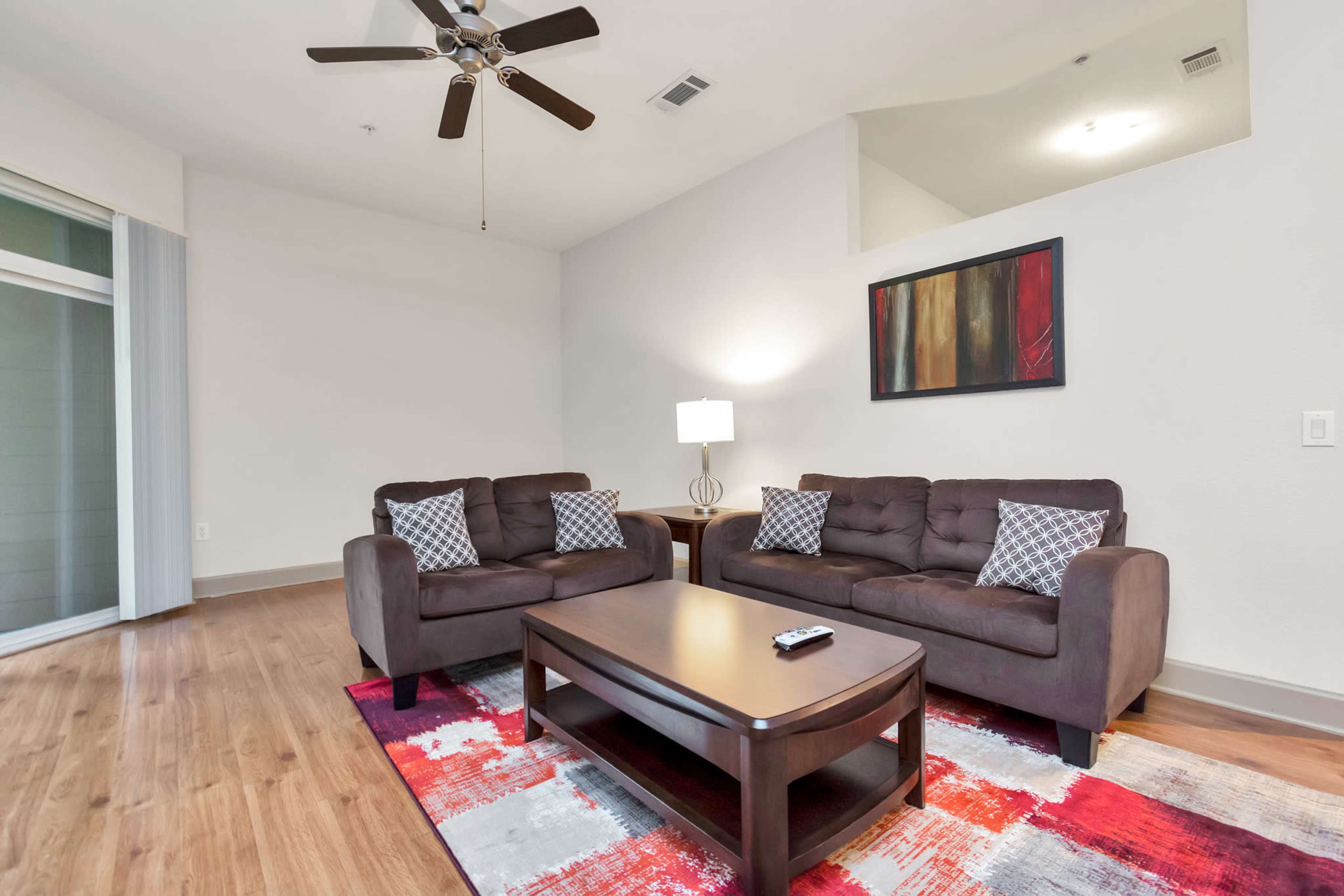 A modern living room featuring two brown sofas, a coffee table, a lamp, and a colorful area rug.
