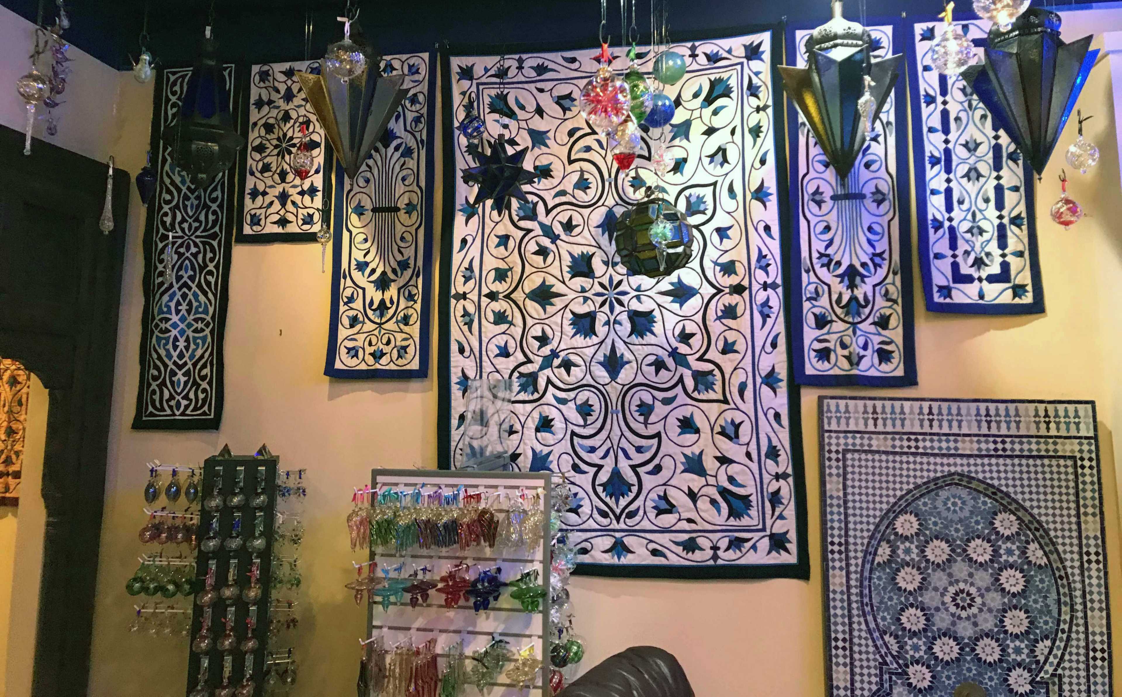 The image shows a decorative wall adorned with blue and white patterned textiles and hanging lanterns, alongside a display rack of various ornaments.