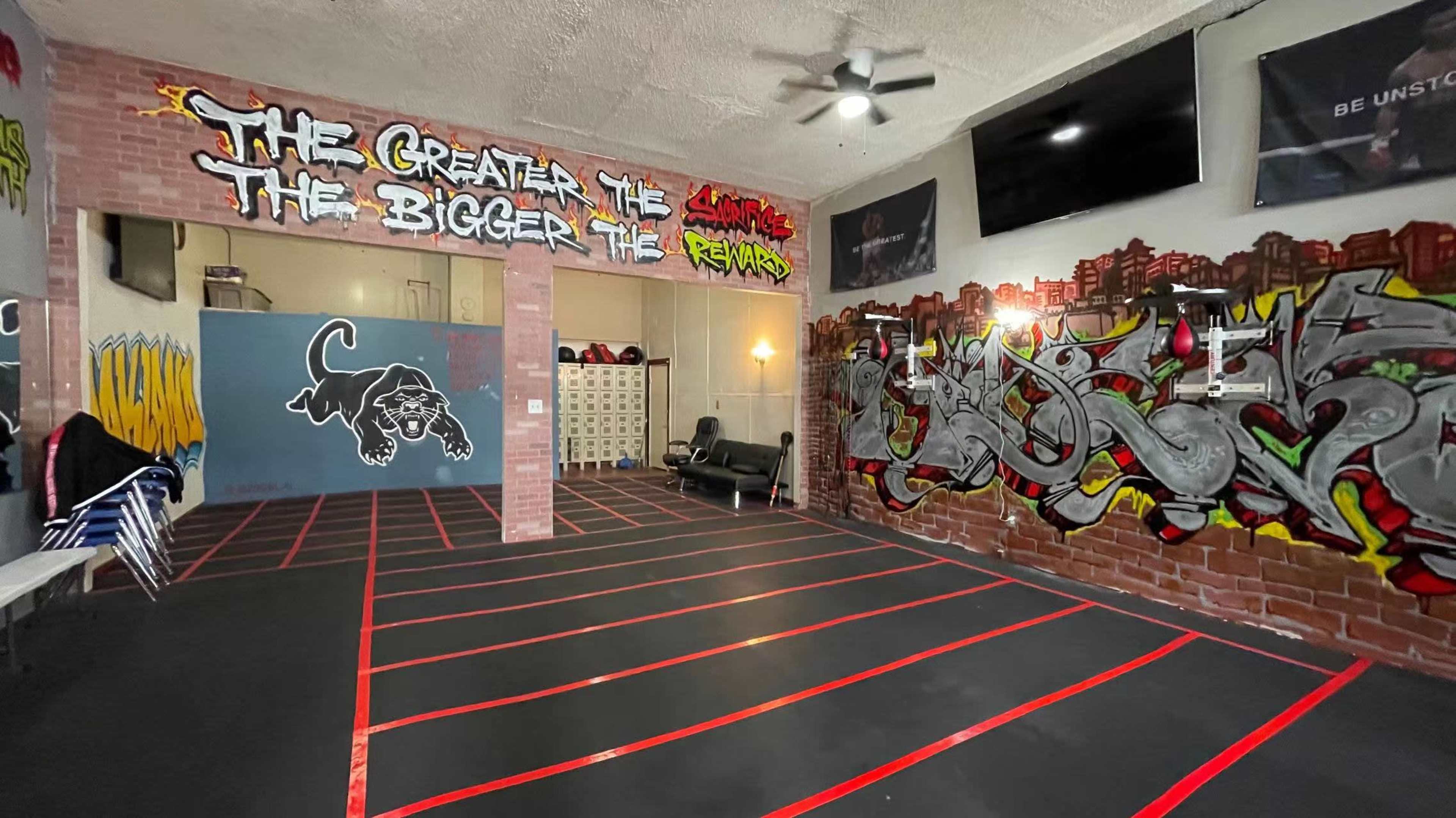 A workout space with red tape marking specific areas on the black floor, surrounded by graffiti-covered walls and motivational quotes.