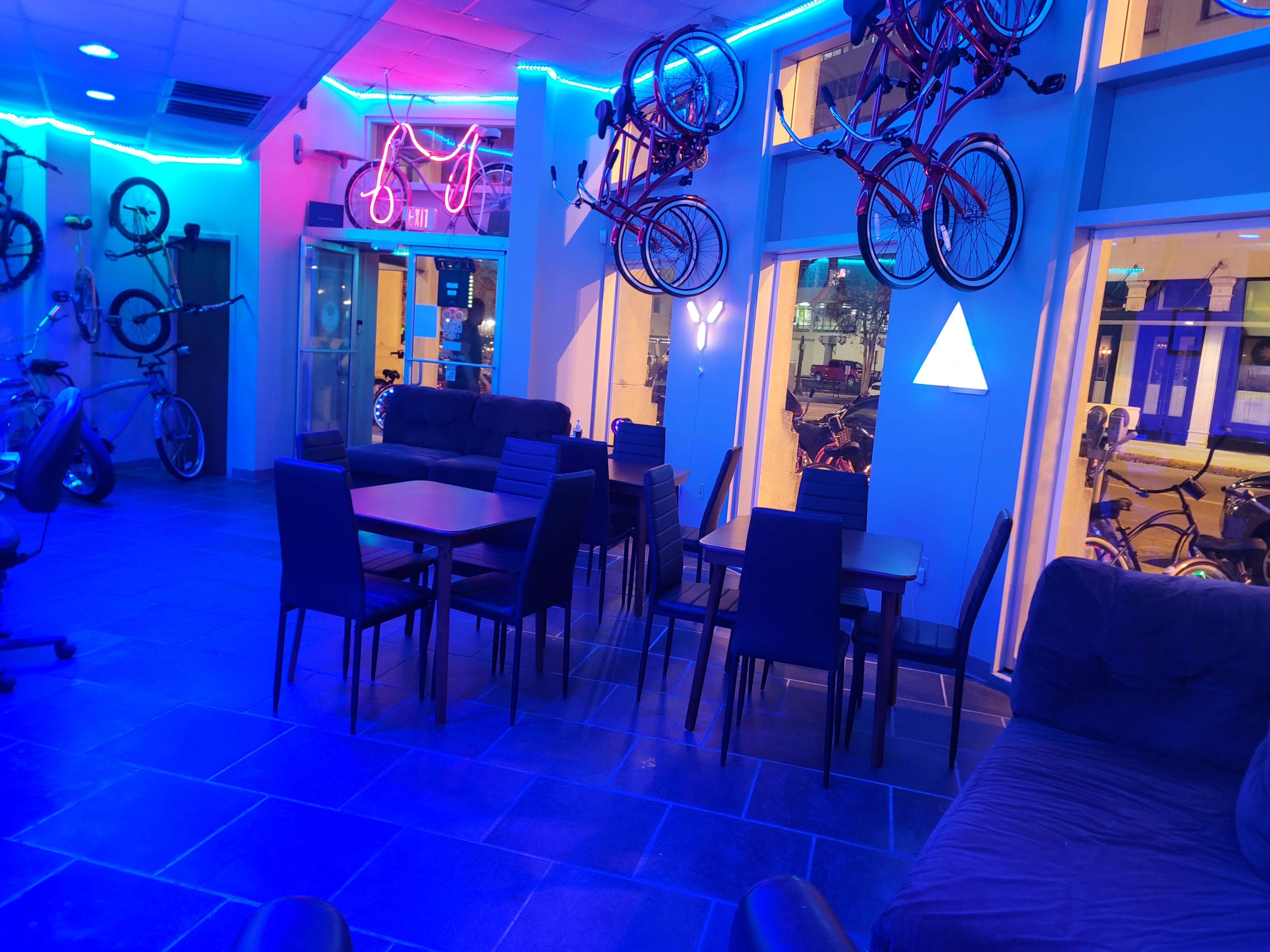 A modern indoor space featuring several bicycles displayed on the walls, a seating area with tables and chairs, and blue neon lighting.