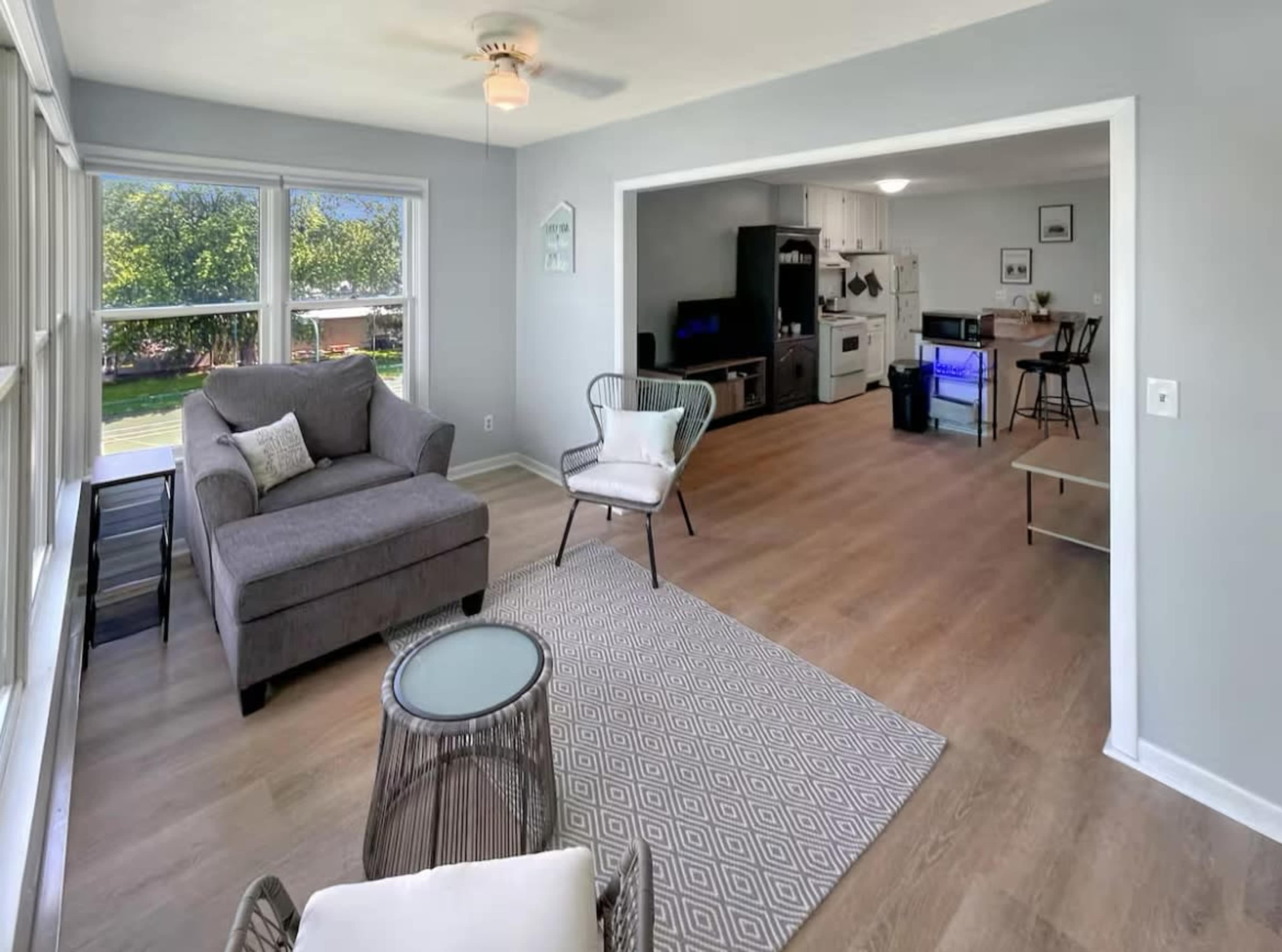 The image shows a bright living room with a gray couch, a coffee table, and an open kitchen area visible in the background.