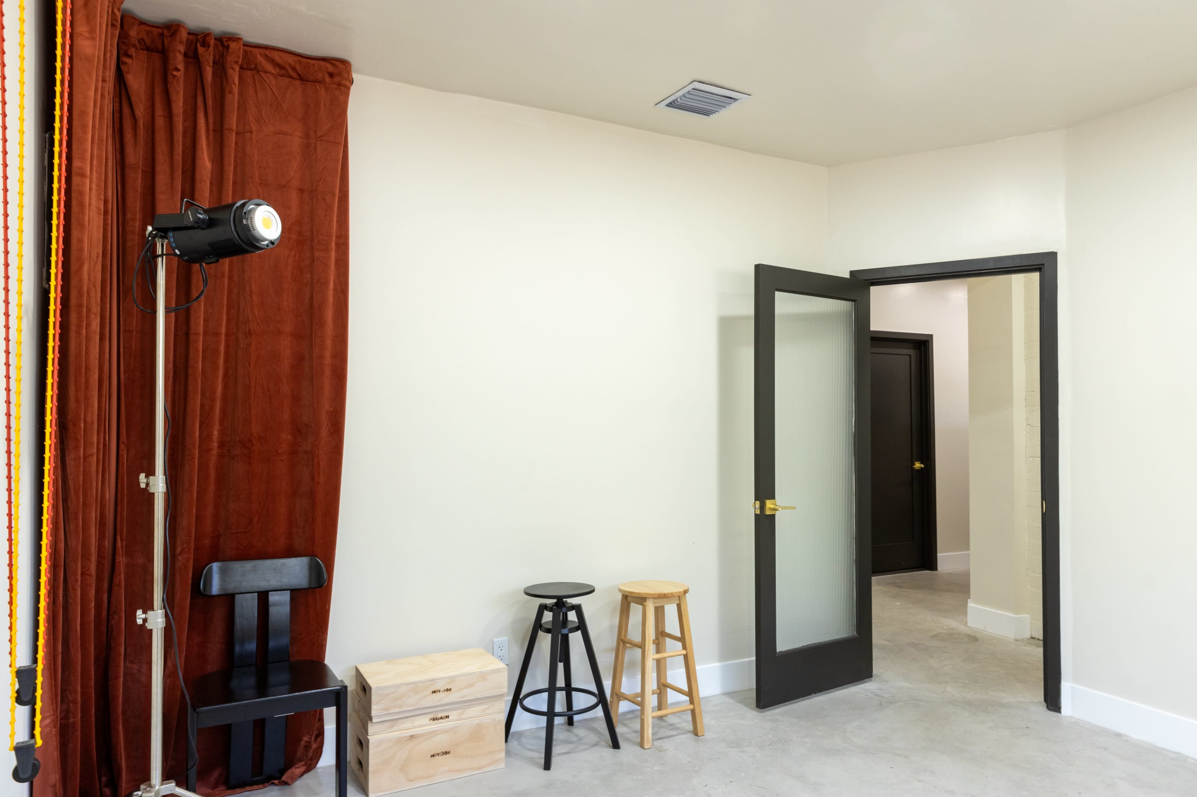 A room with a red curtain, a black stool, a wooden stool, and an open door leading to another space.