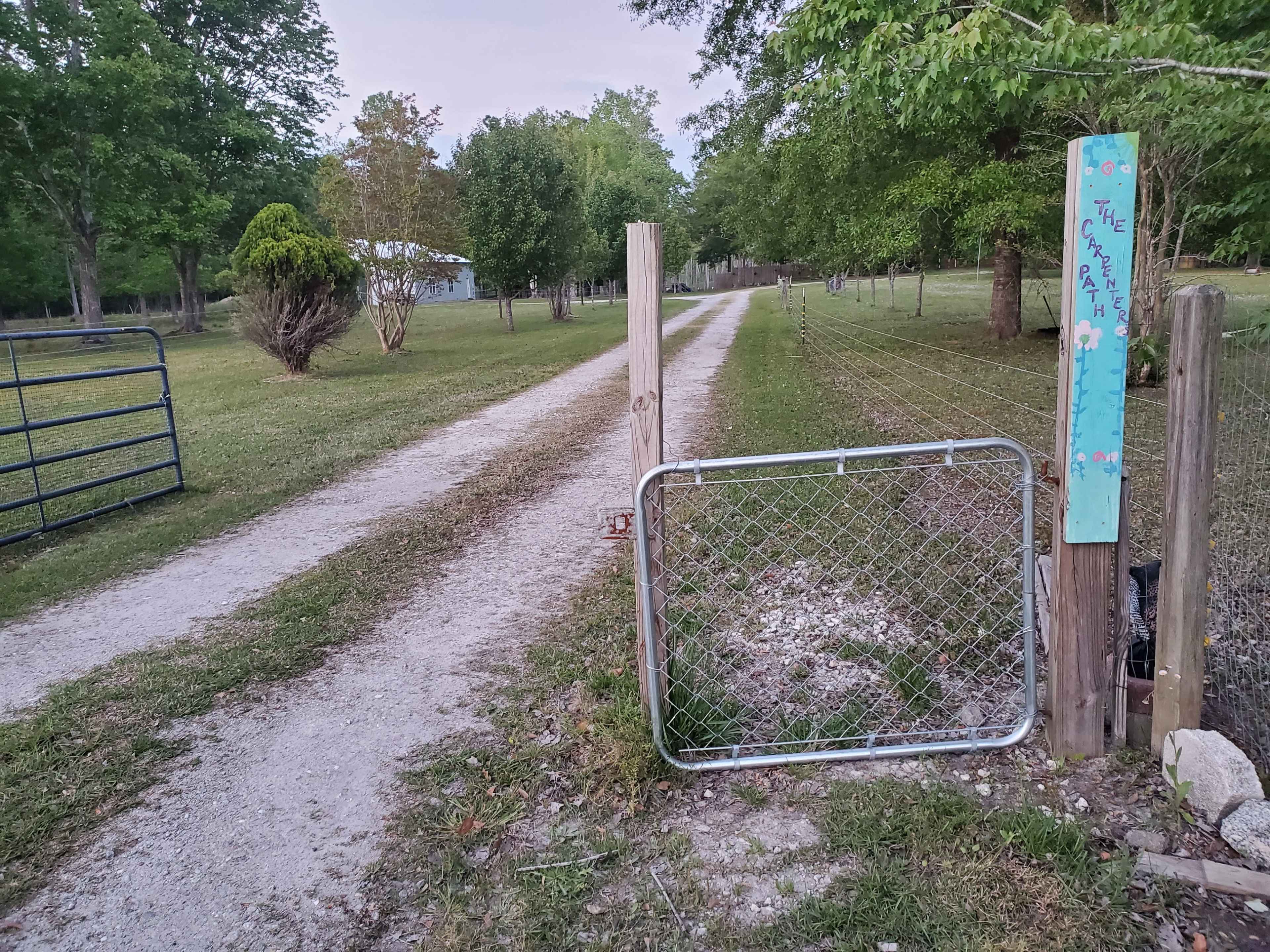 A gravel path leads through an open gate into a tree-lined area.