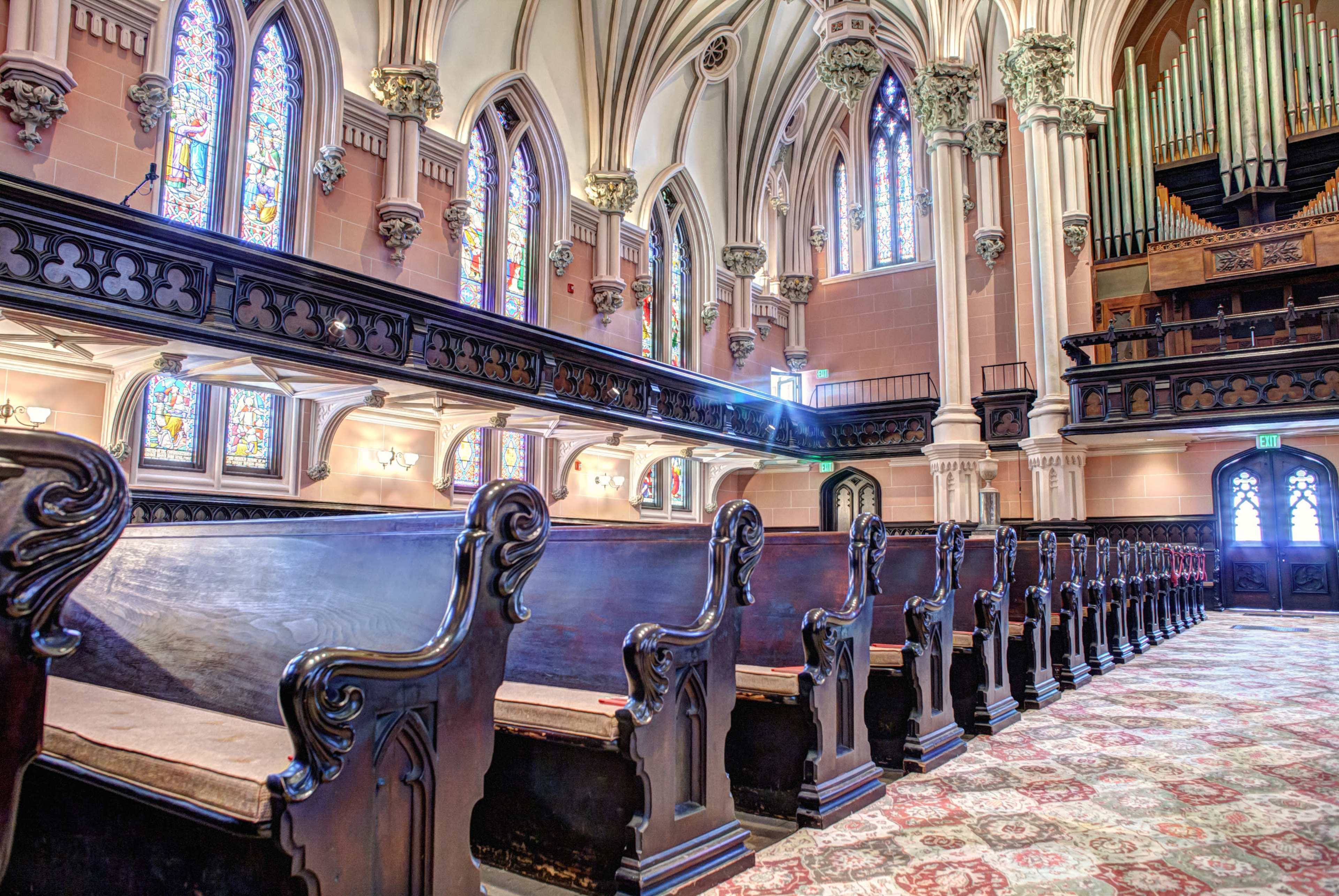 The image shows the interior of a church with stained glass windows, ornate wooden pews, and a large pipe organ.