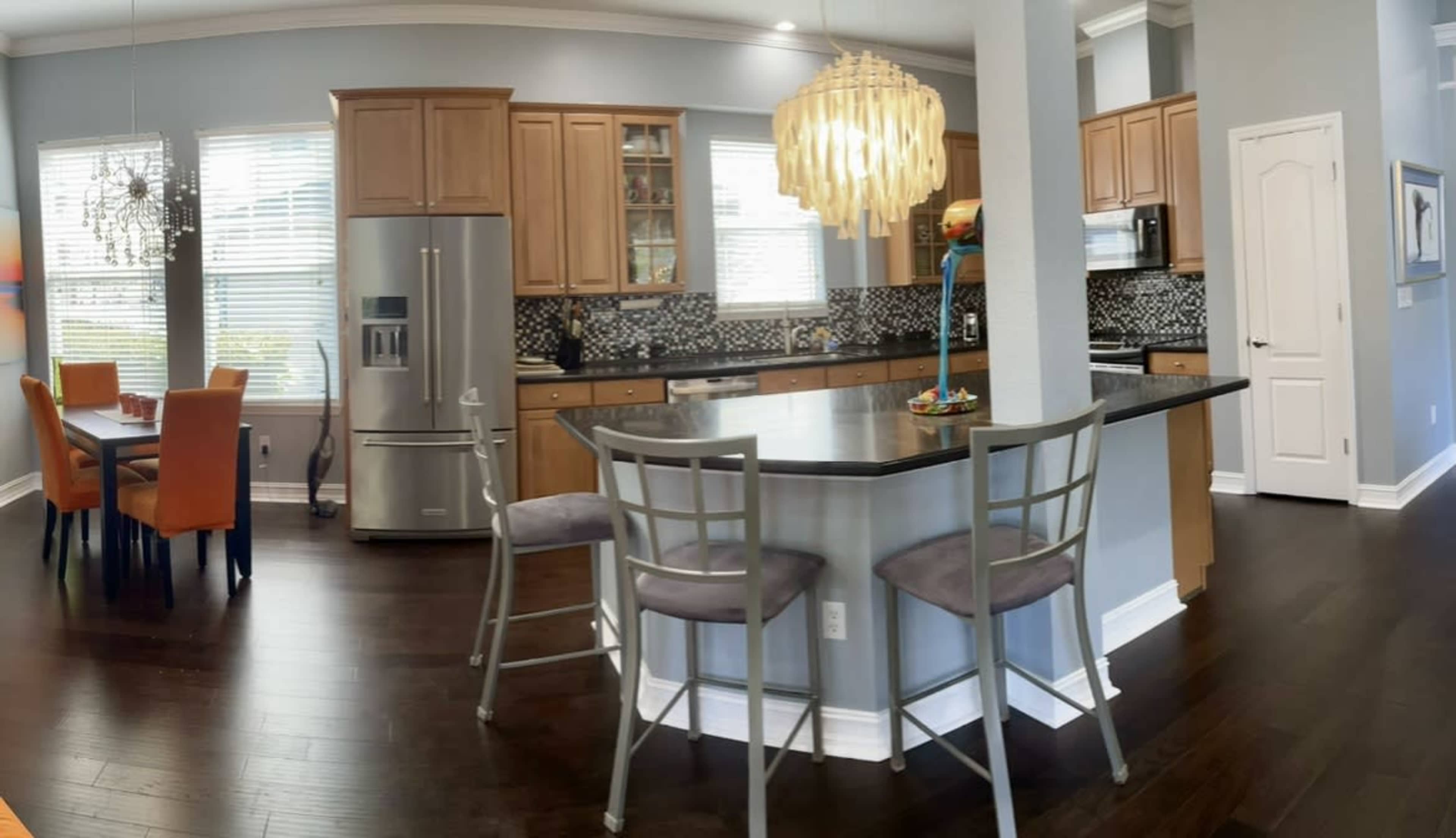 A modern kitchen with wooden cabinets, stainless steel appliances, and a breakfast bar with stools, adjacent to a dining area featuring a table and chairs.