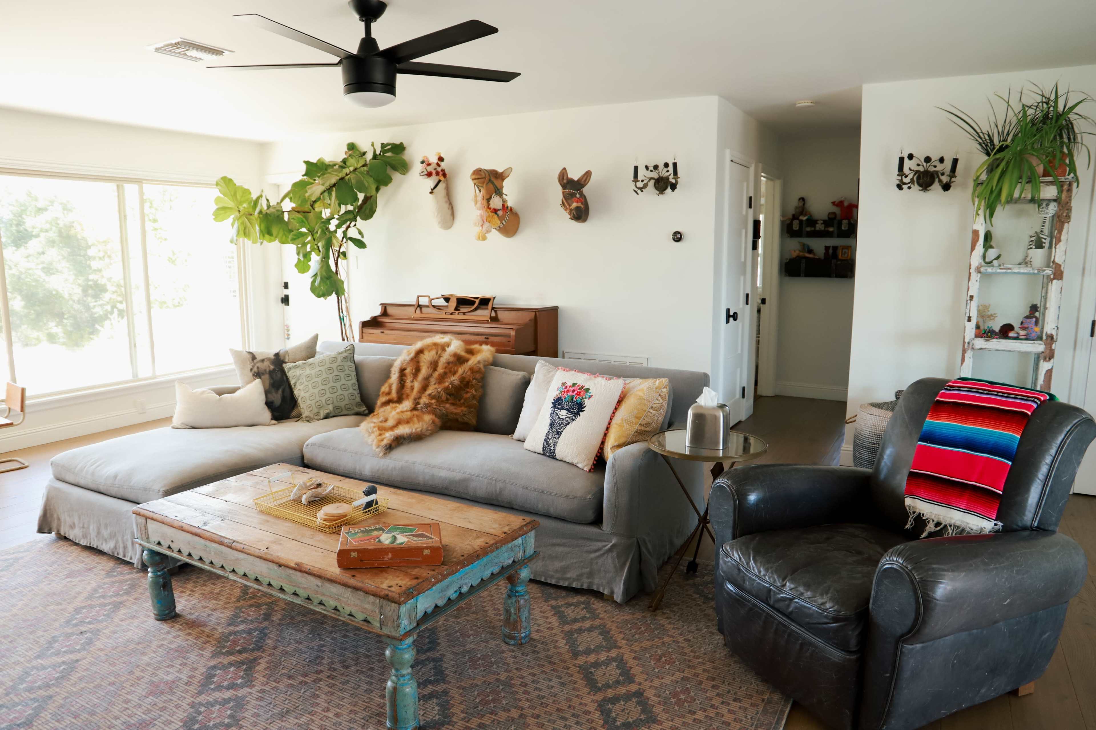A living room features a large sectional sofa, a wooden coffee table, and a piano, adorned with various decorative items and plants.