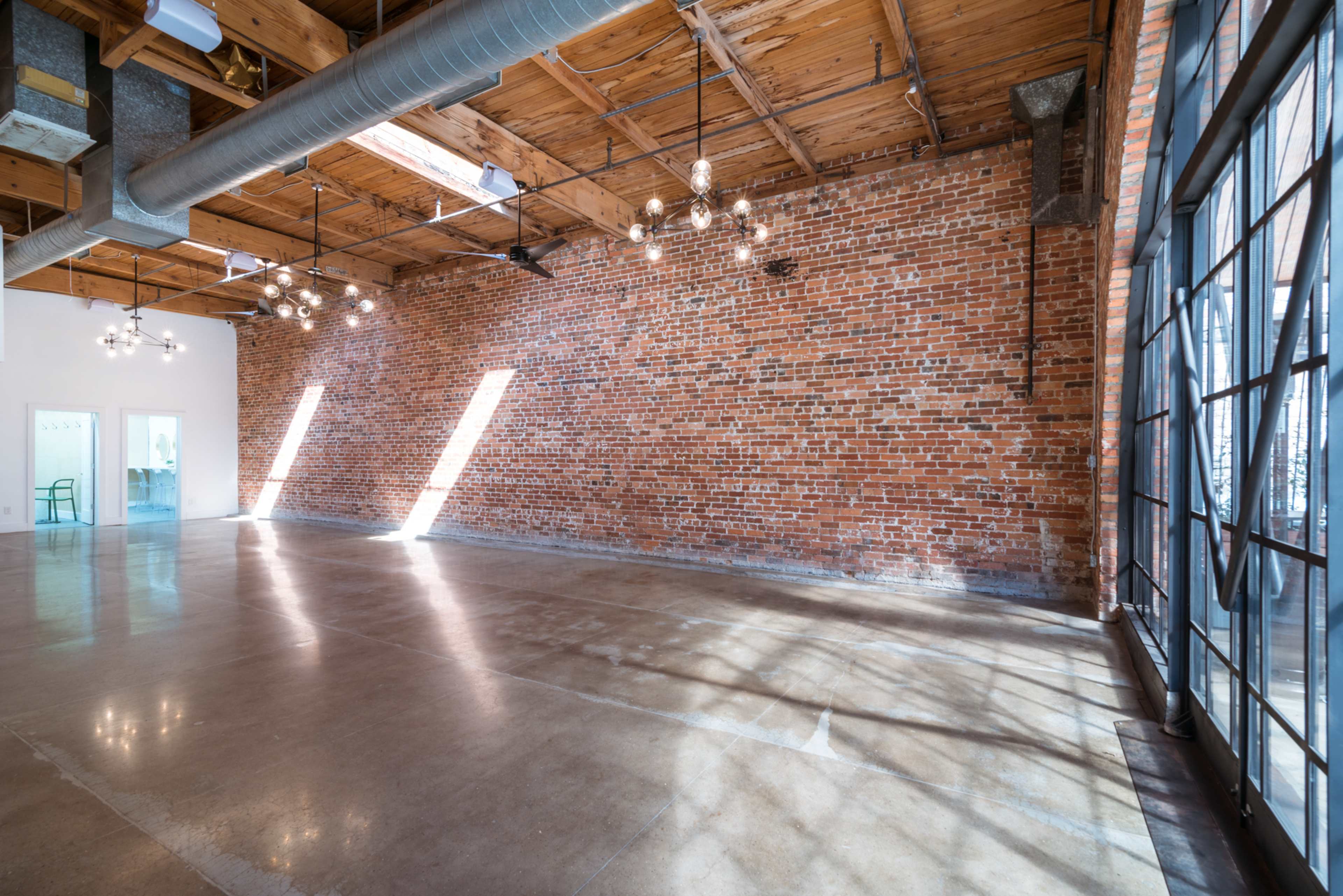 An empty industrial-style interior with exposed brick walls, a polished concrete floor, and large windows allowing natural light to enter.