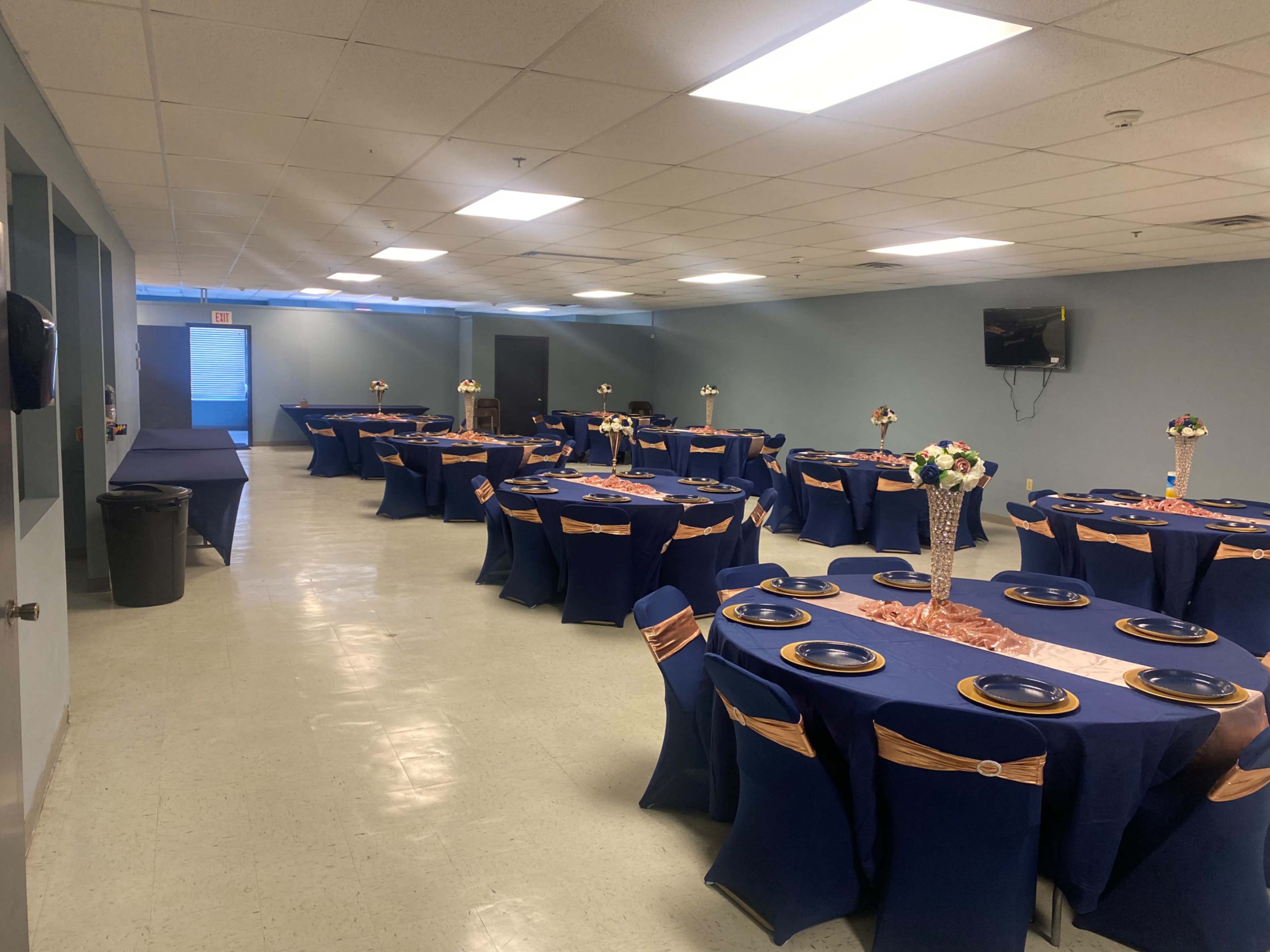 A banquet hall set up with multiple round tables adorned with navy blue tablecloths and centered flower arrangements.