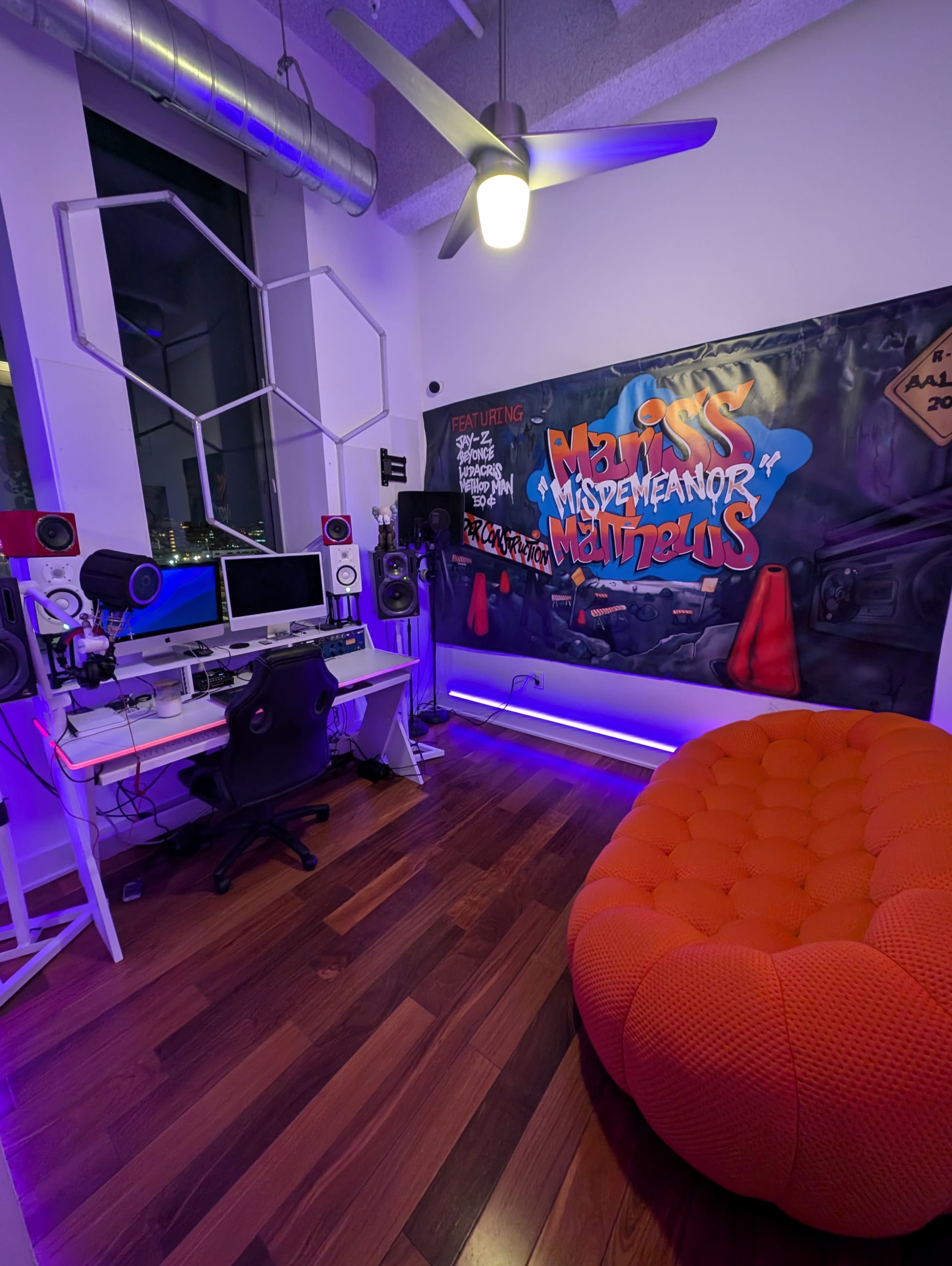 The image shows a modern music studio with a desk equipped with audio gear, a large orange circular couch, and a colorful graffiti-style mural on the wall.