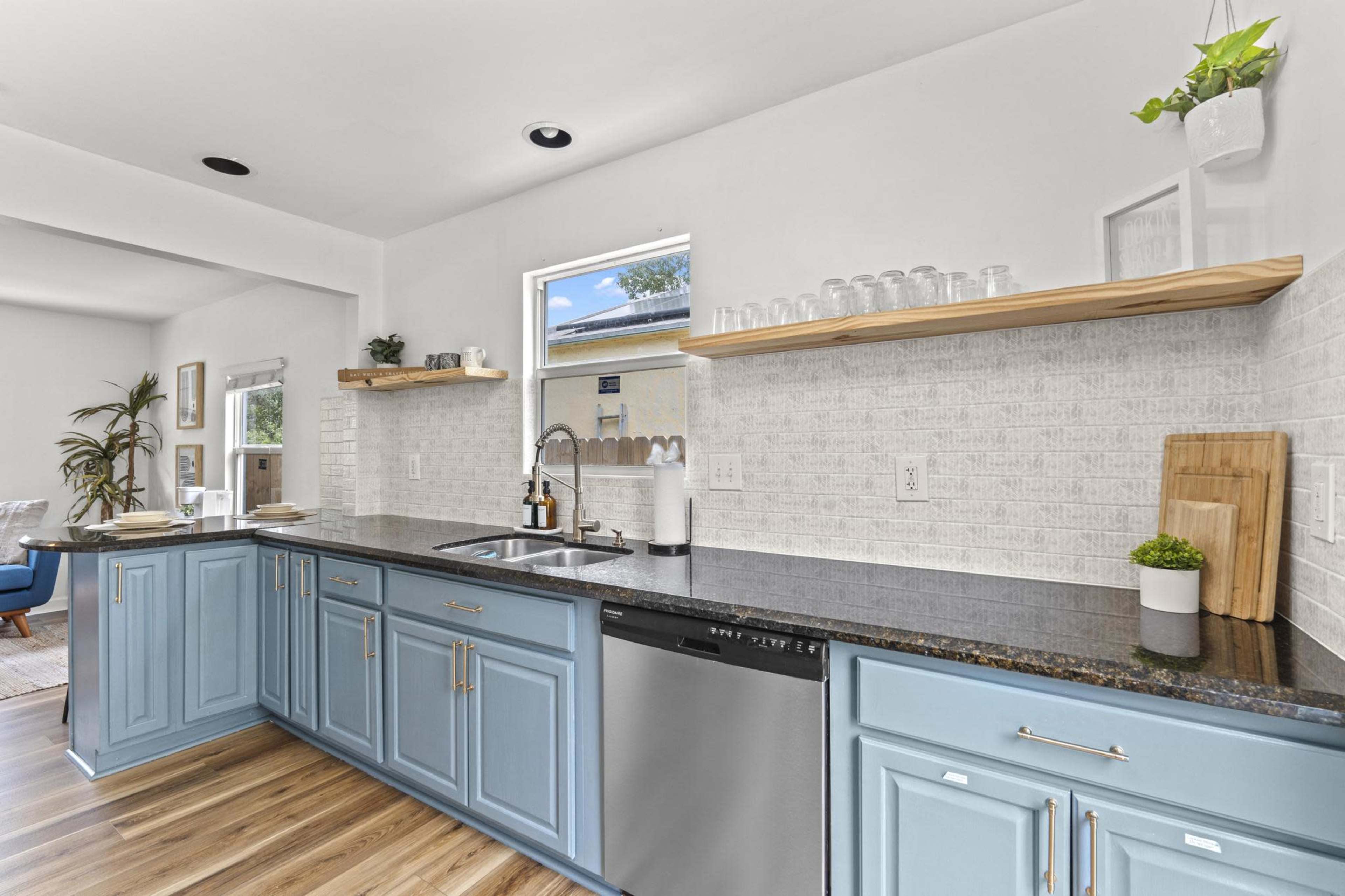 A modern kitchen features blue cabinets, a stainless steel sink, and open shelving with decorative items against a light-colored wall.