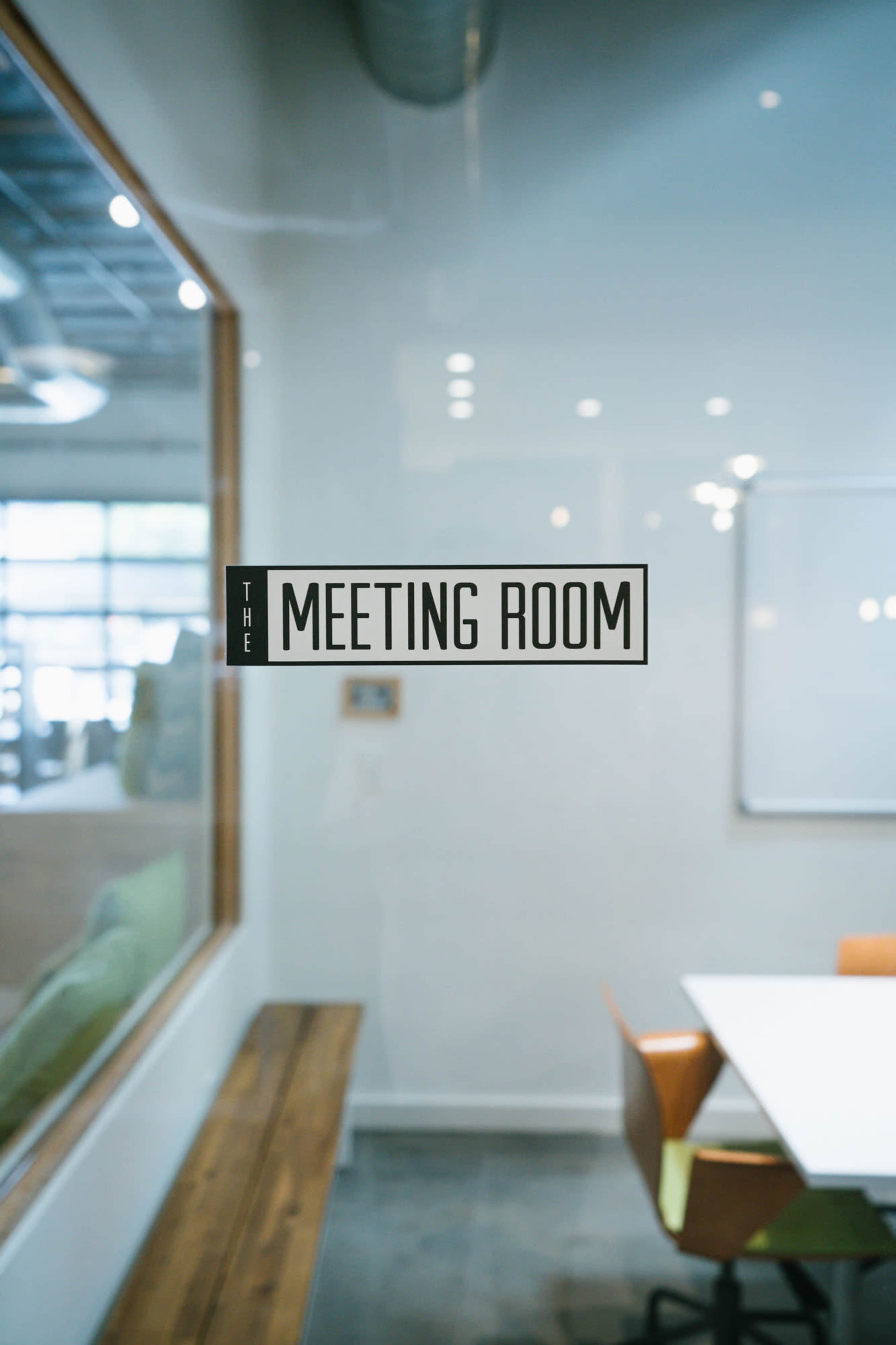 A glass-walled meeting room features a table and colorful chairs, with a sign indicating "THE MEETING ROOM."