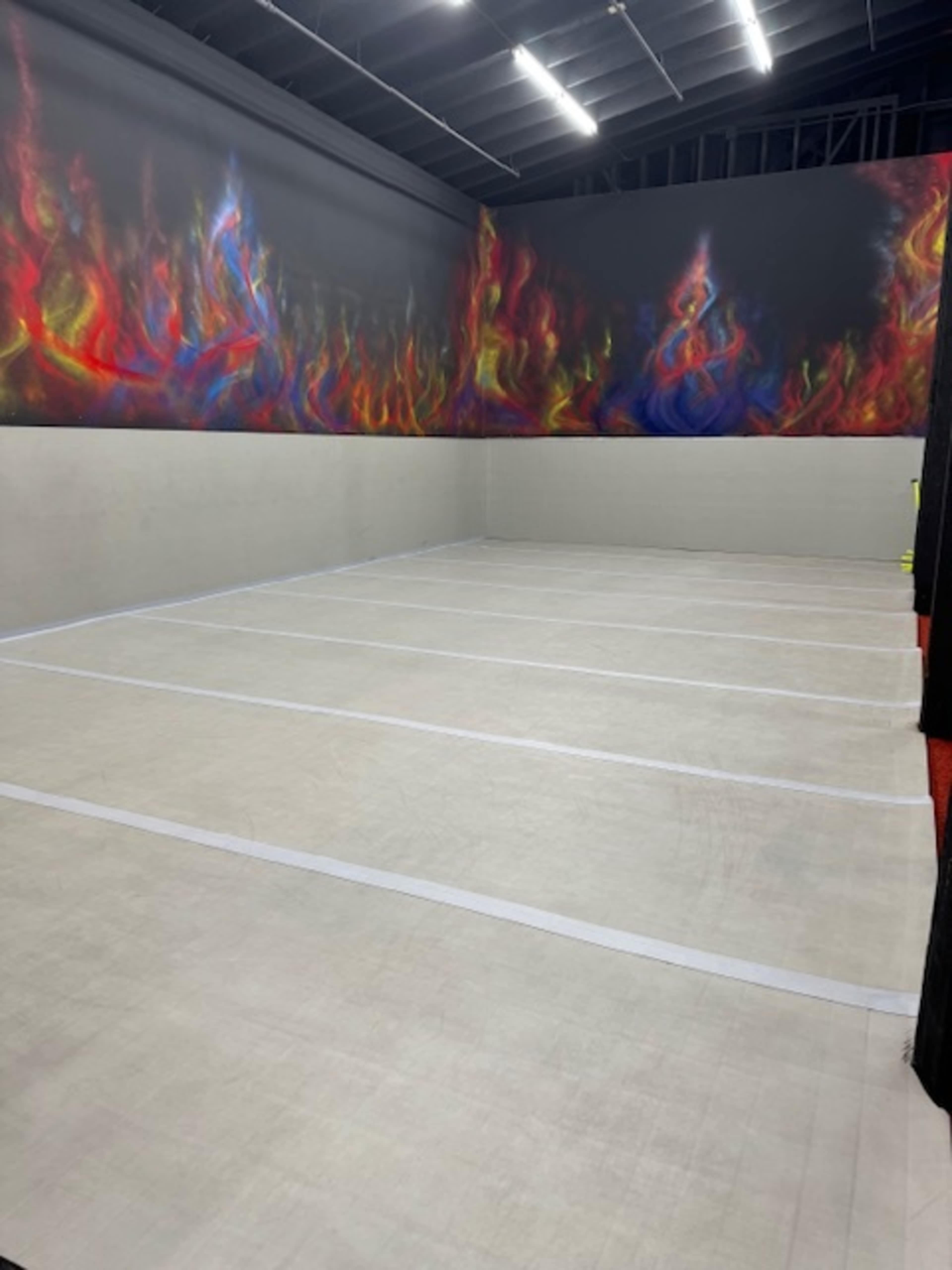 An indoor sports court with a colorful flames mural on one wall and a plain, empty playing surface.