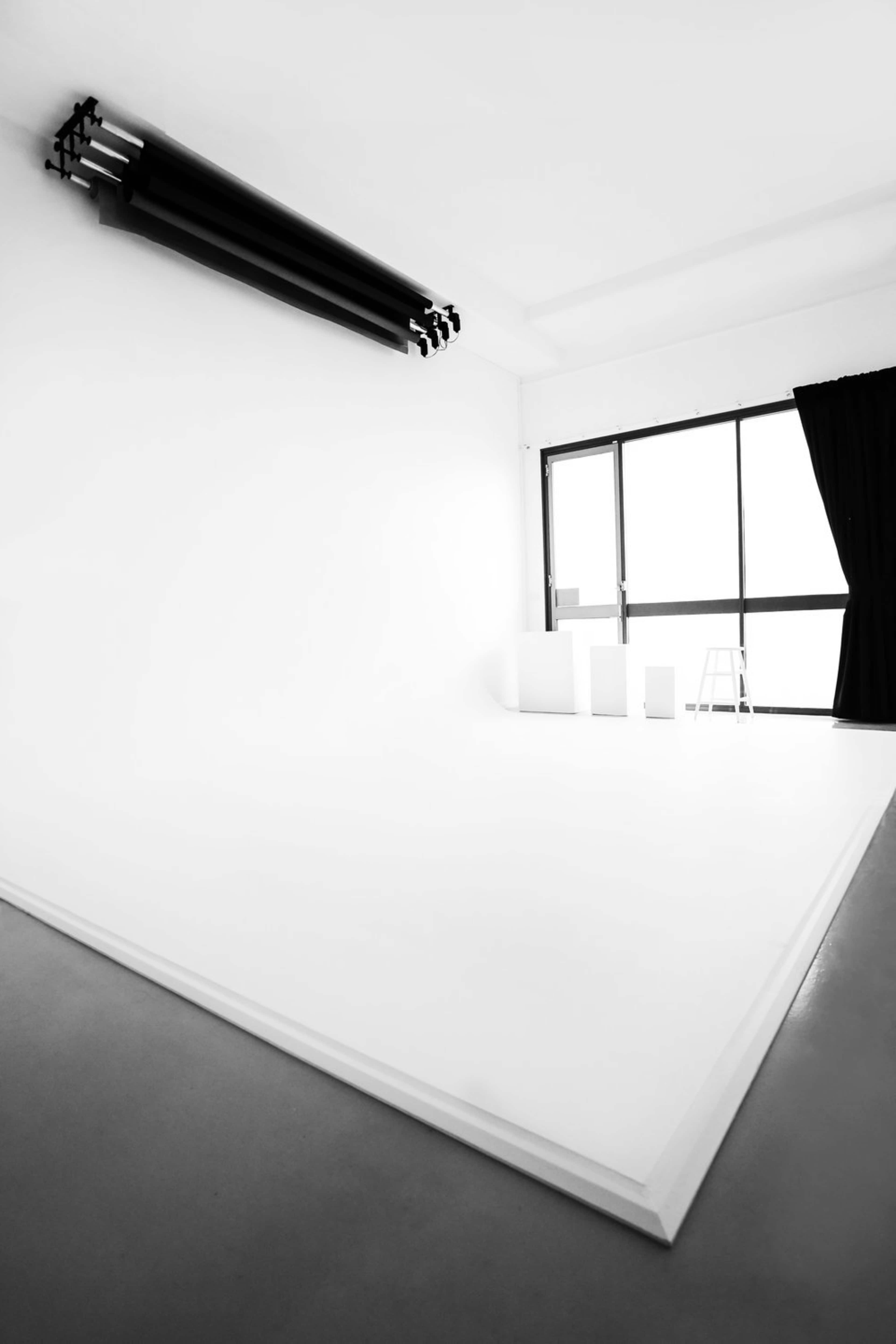 A minimalist studio space with a large white floor, black curtains, and a window revealing bright light.