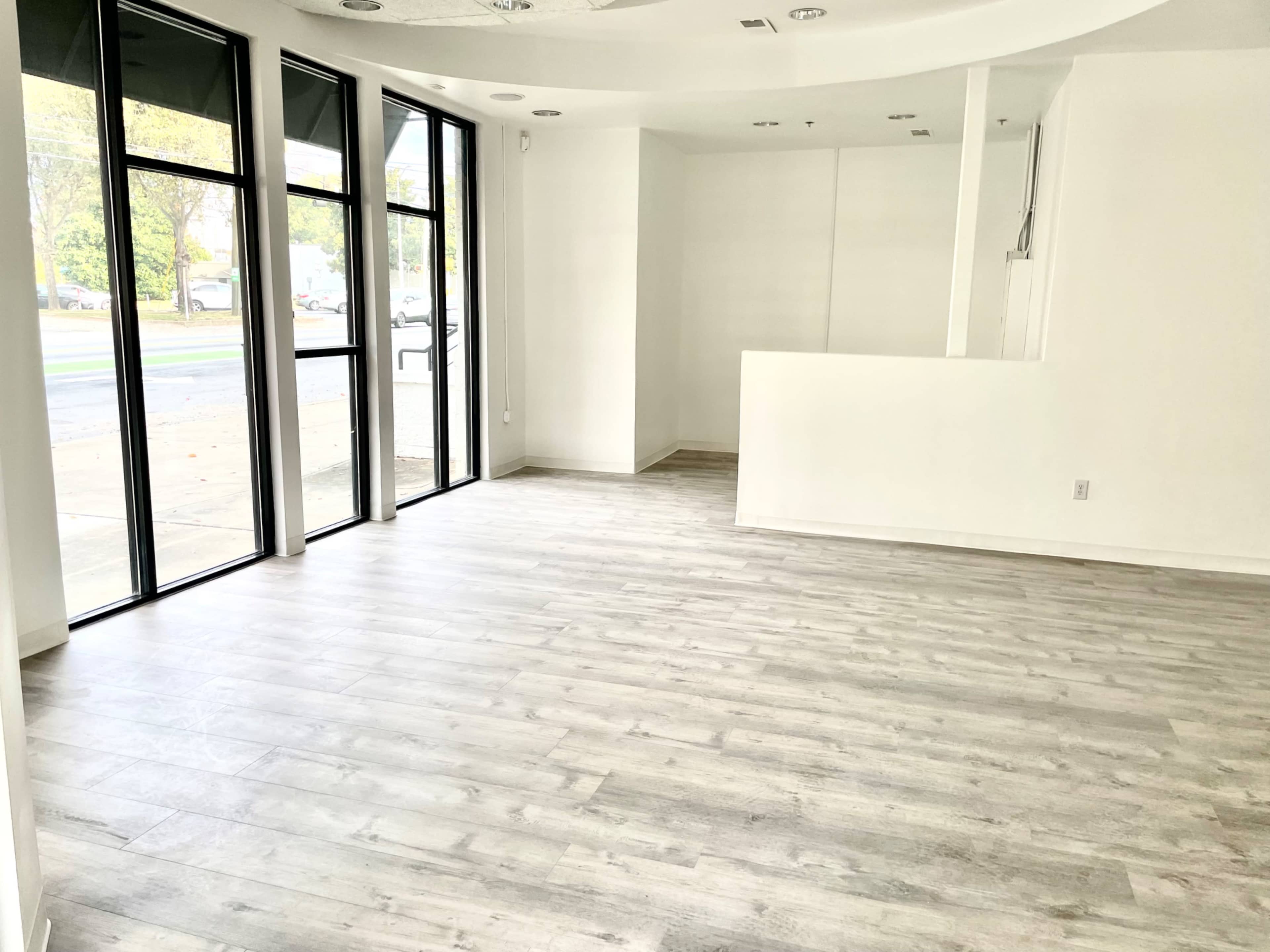 An empty, well-lit commercial space with large windows and a light-colored wooden floor.