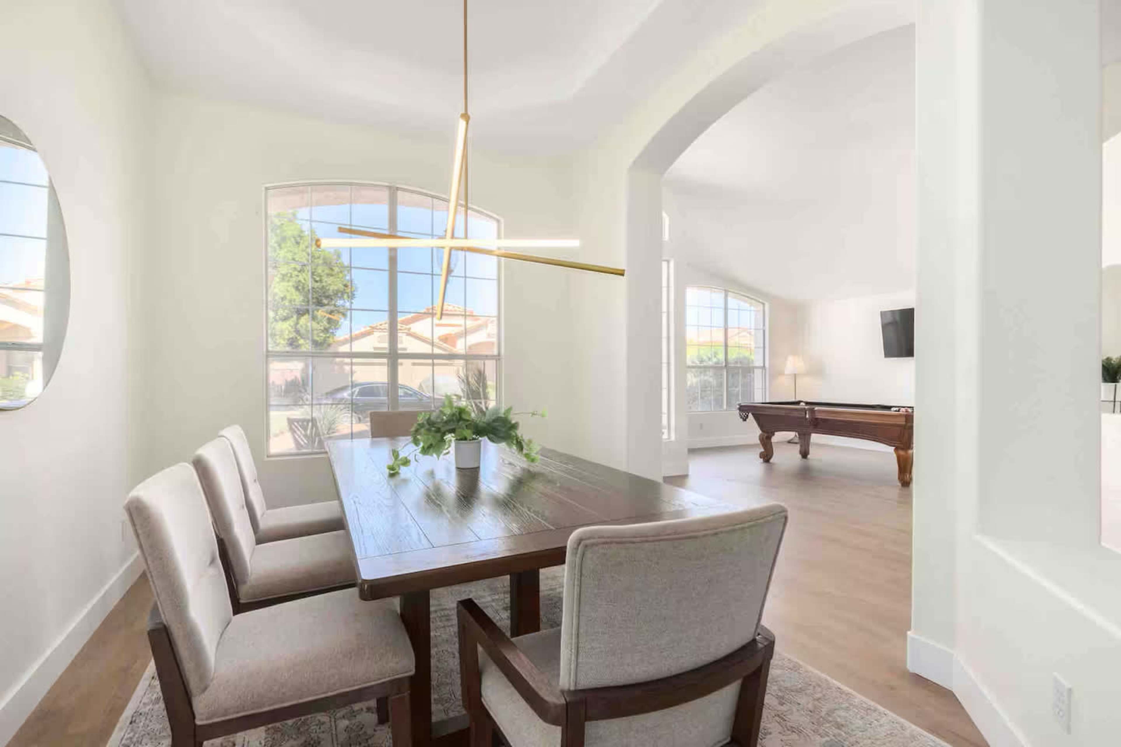 A dining area features a wooden table with four chairs, a light fixture above, and large windows allowing natural light to enter.