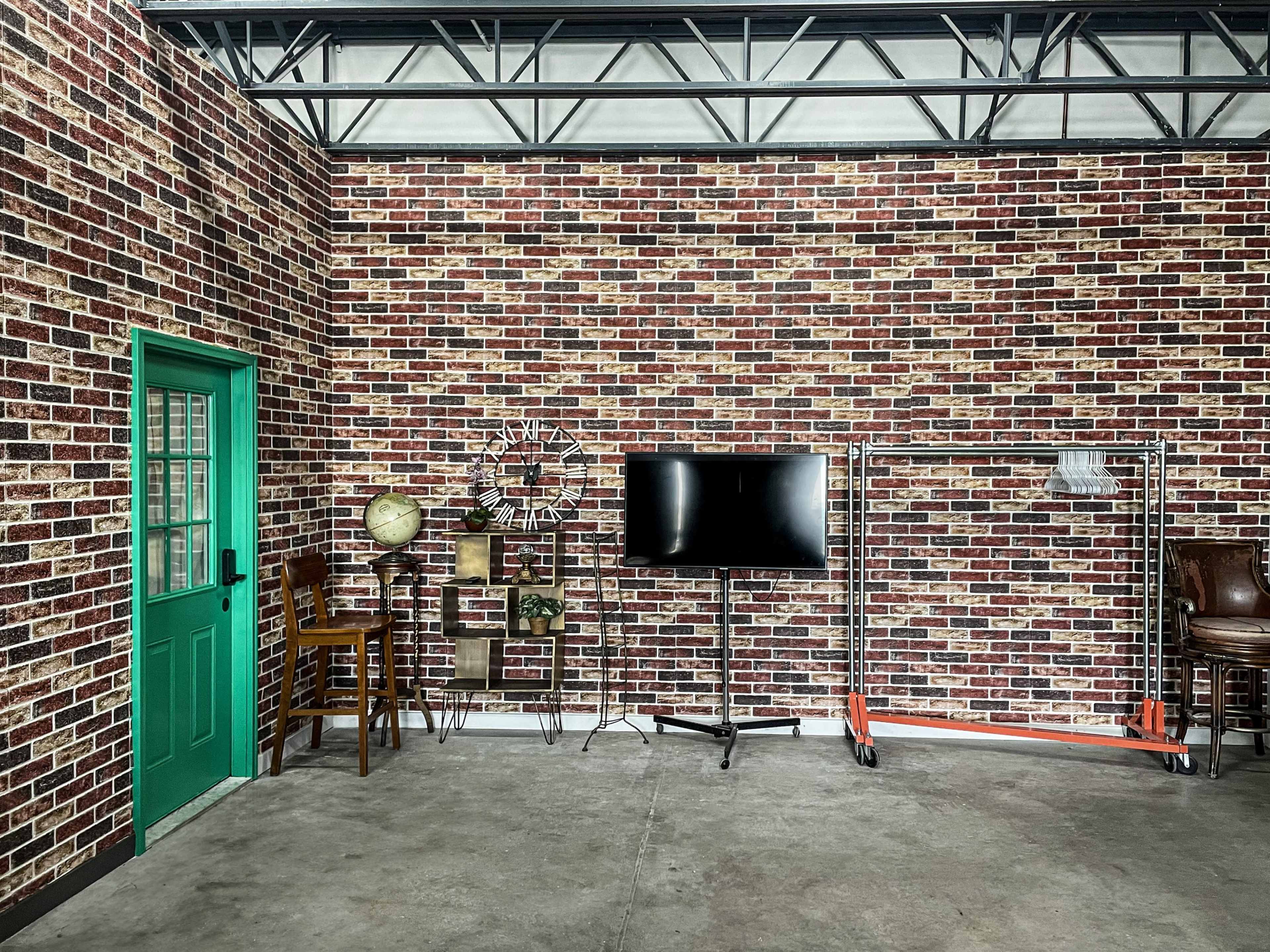 A room with a brick-patterned wall, a green door, a television stand, a globe on a shelf, and a clothing rack.