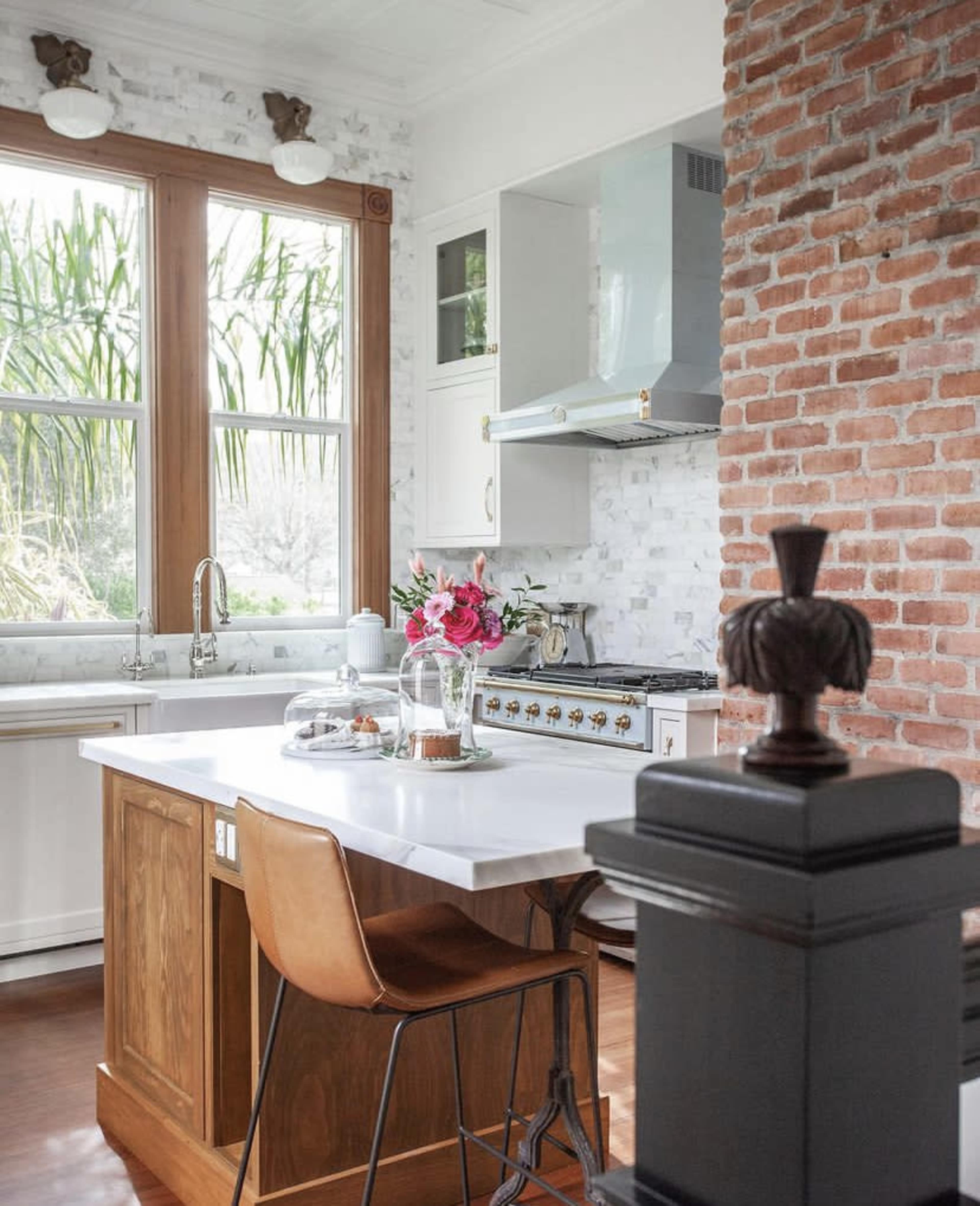 A kitchen features a marble countertop, a vintage stove, and a window with lush greenery outside.