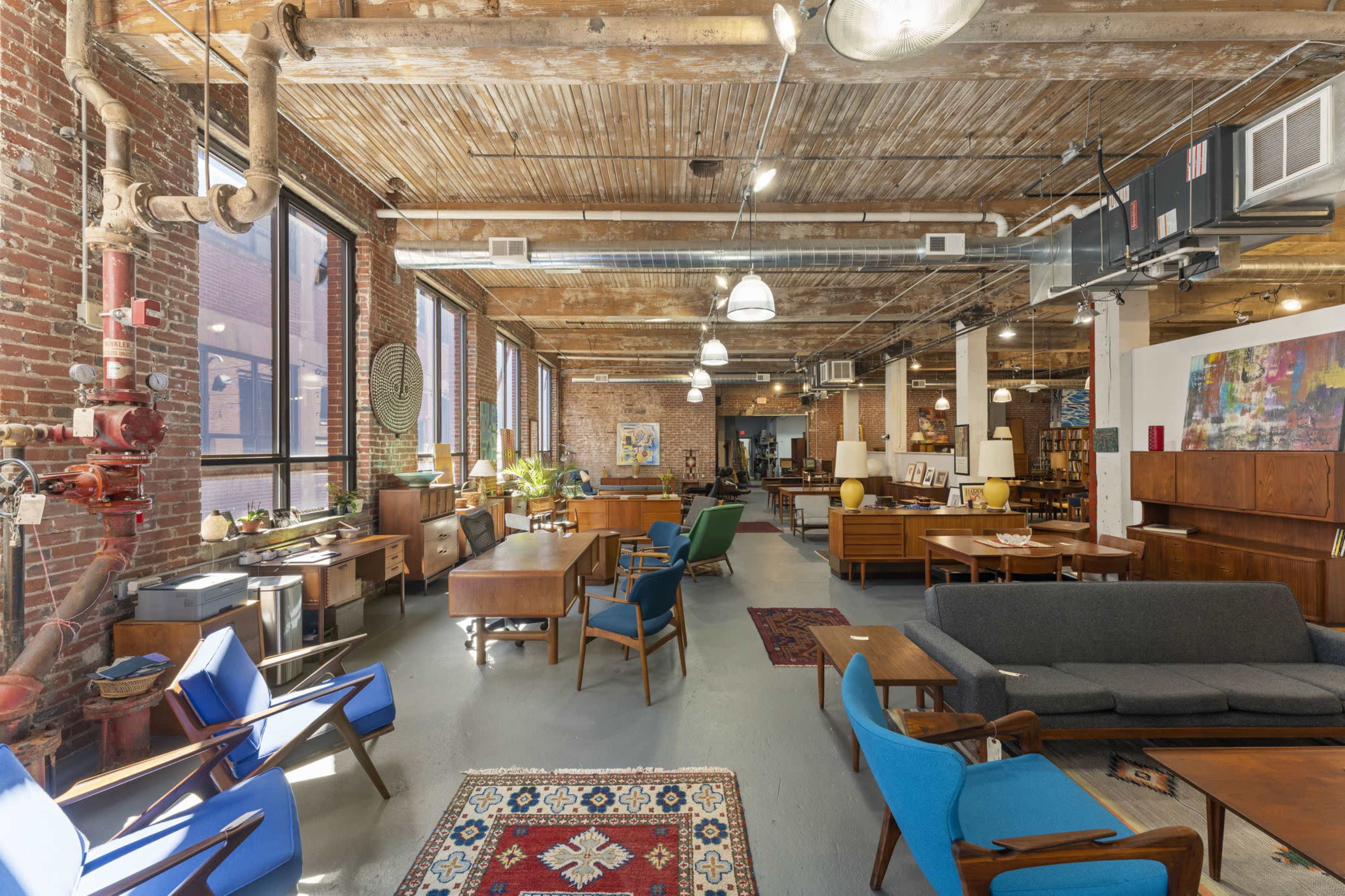 A spacious, industrial-style interior filled with various vintage furniture pieces, wooden beams, and brick walls.