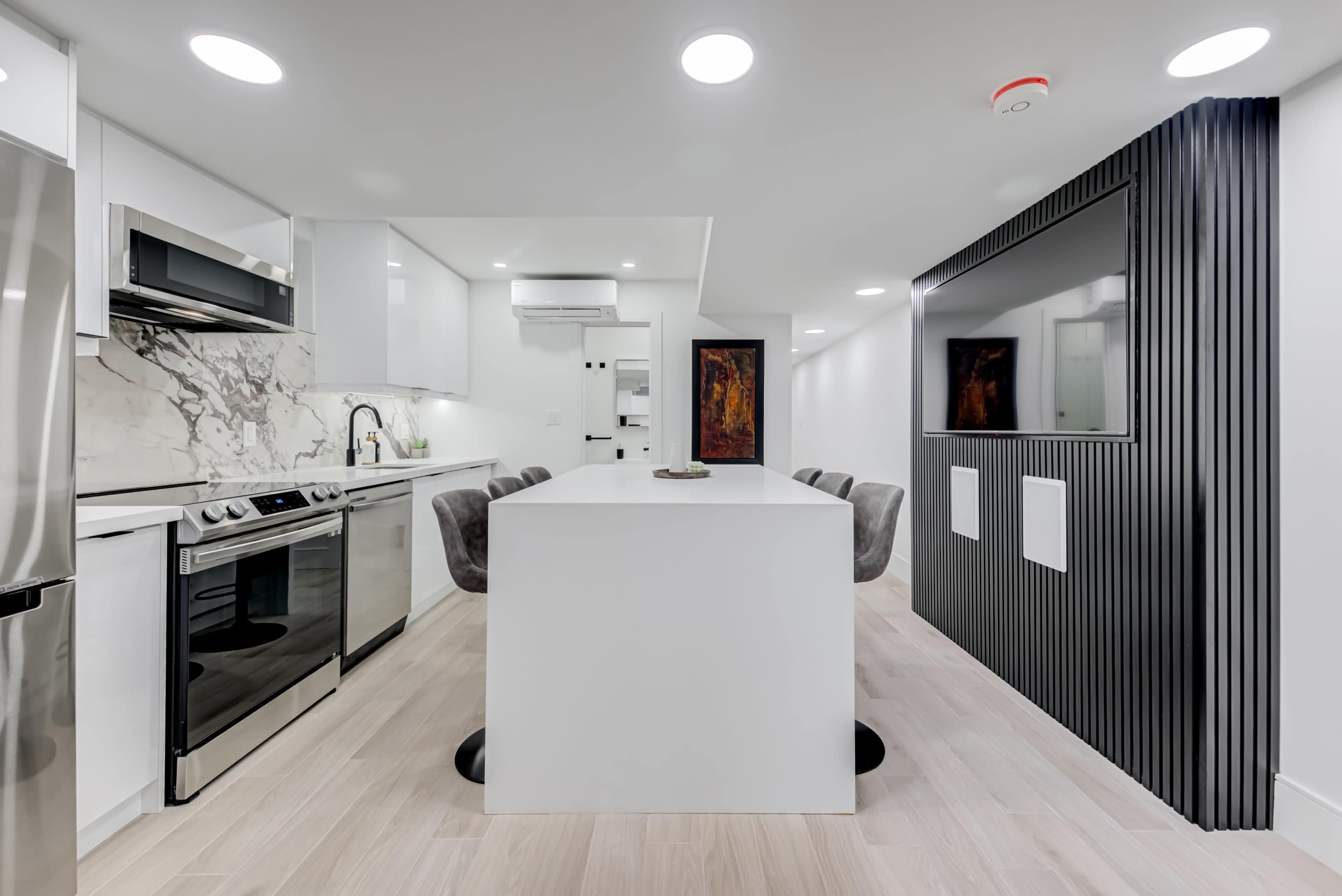 A modern kitchen features a central island with seating, stainless steel appliances, and sleek cabinetry against a marble backsplash.