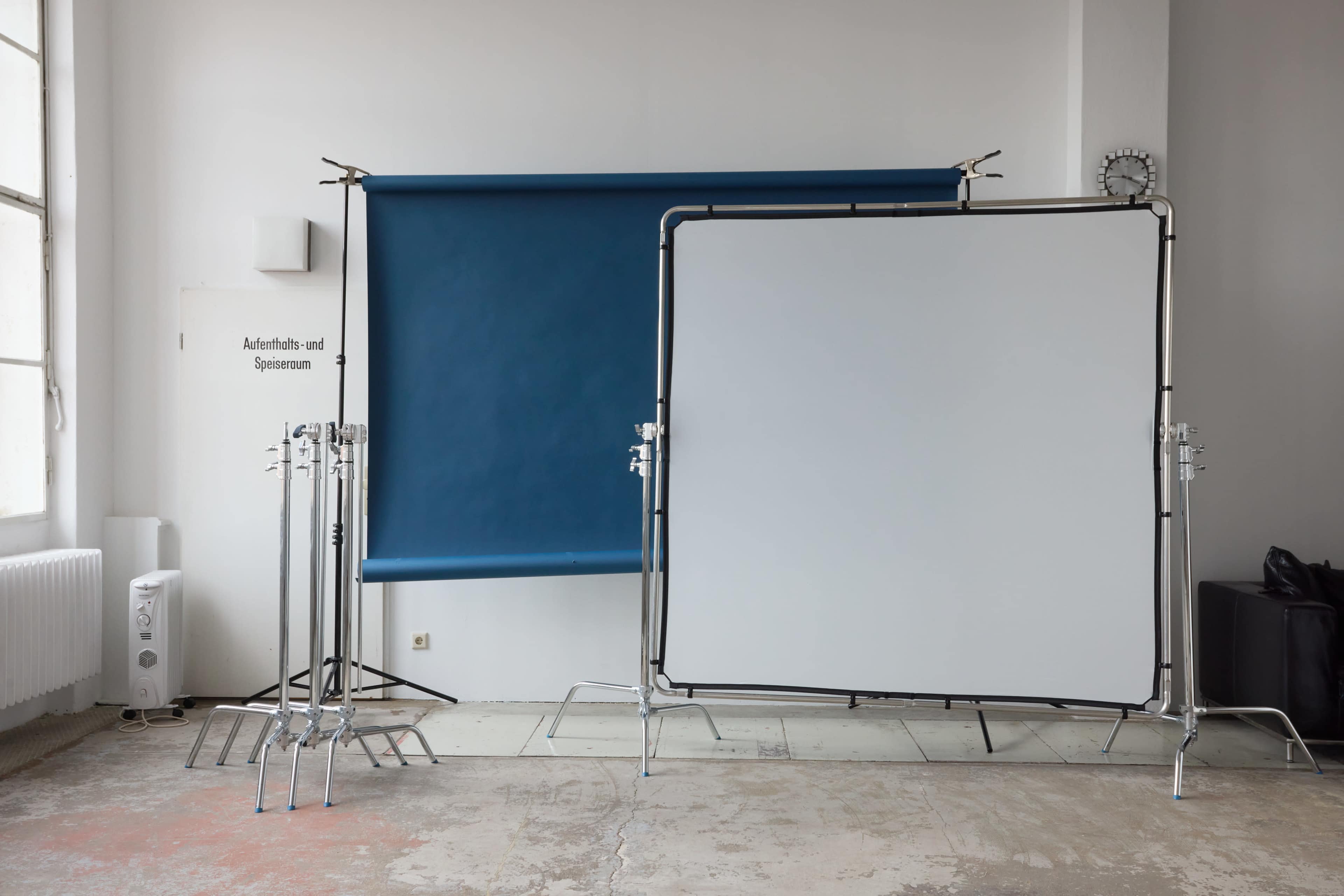 The image shows a photography studio with a blue and a white backdrop set up on metal frames, alongside empty light stands.