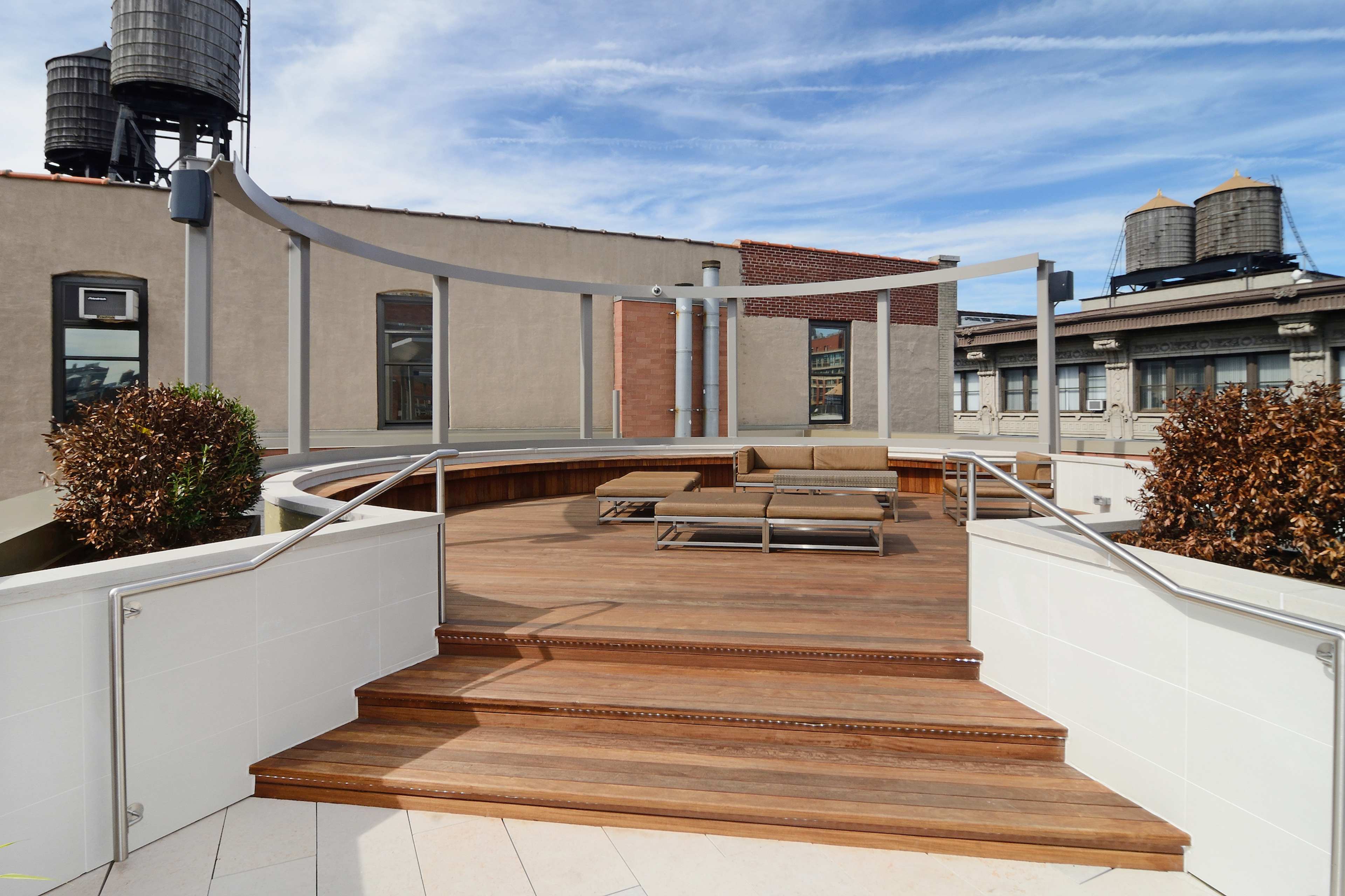 A rooftop terrace with wooden decking, a seating area, and water towers in the background.