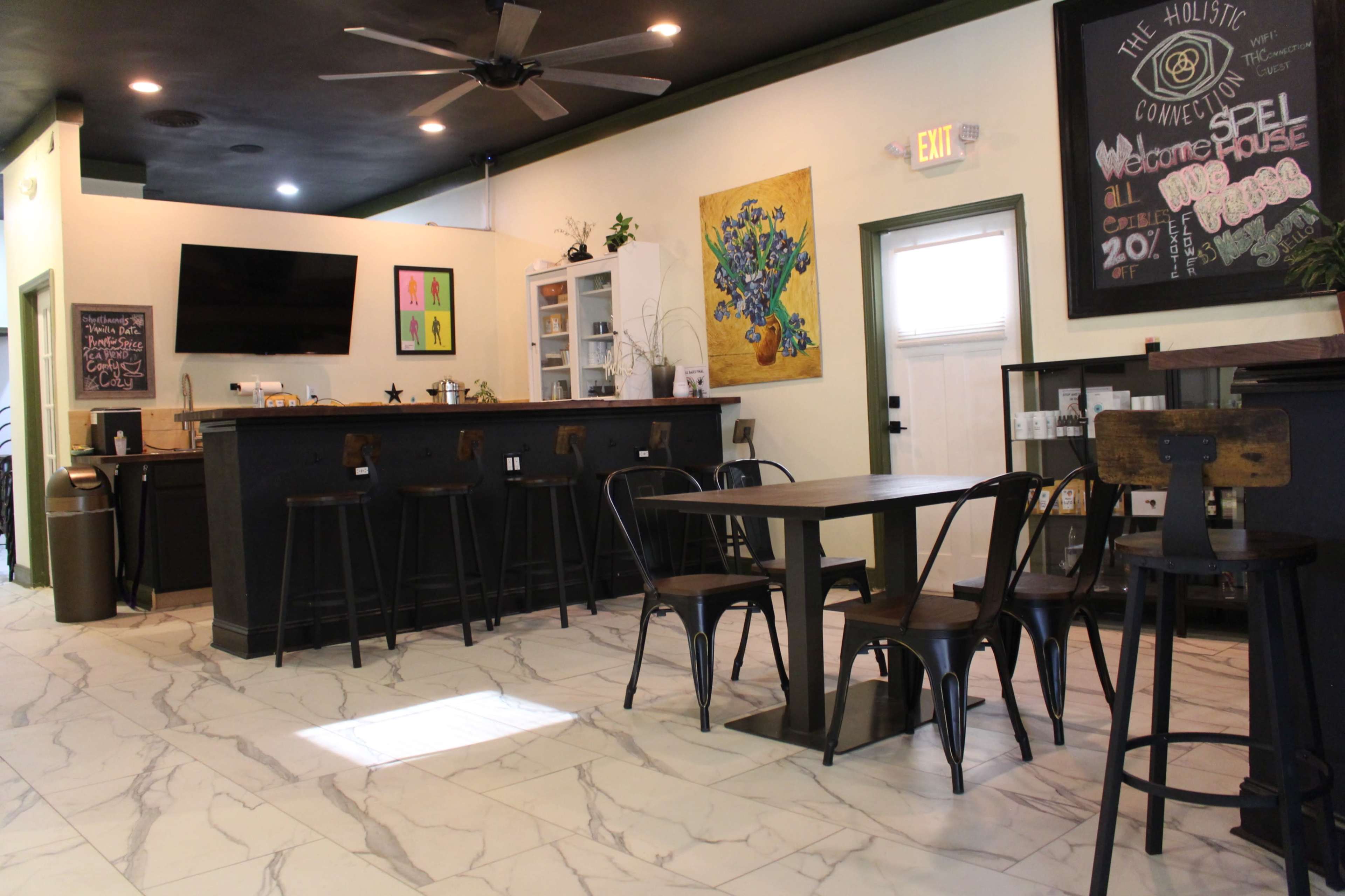 A cozy café interior with a bar counter, several tables, and colorful artwork on the walls.