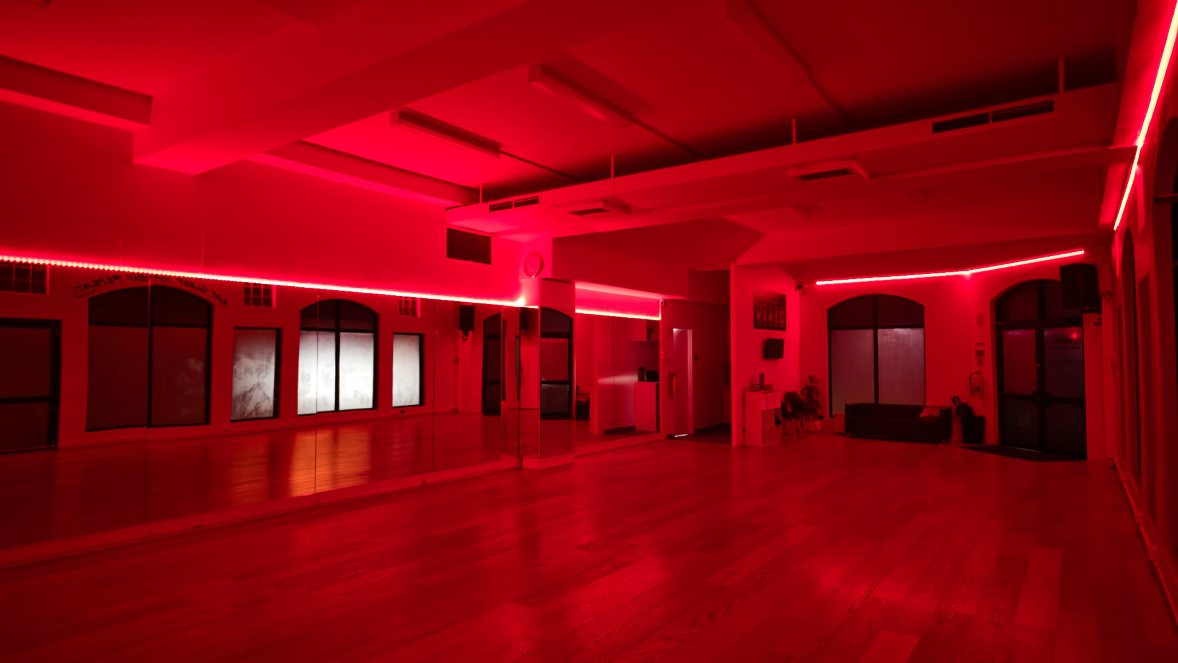 The image shows a dance studio with red LED lighting, polished wooden floors, and large mirrors.