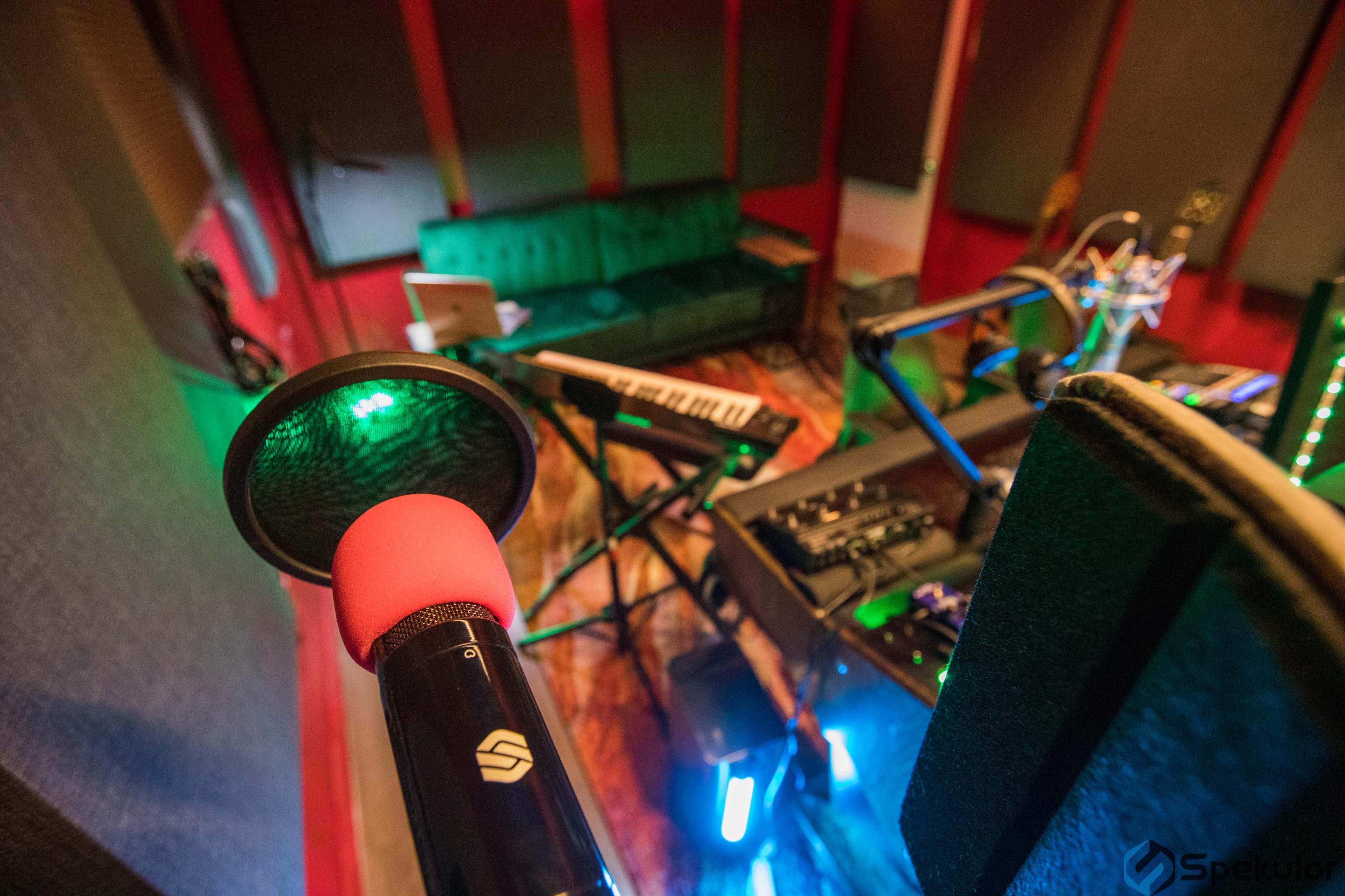 A music recording studio featuring a microphone, a keyboard, and a green couch in a room with soundproof walls.