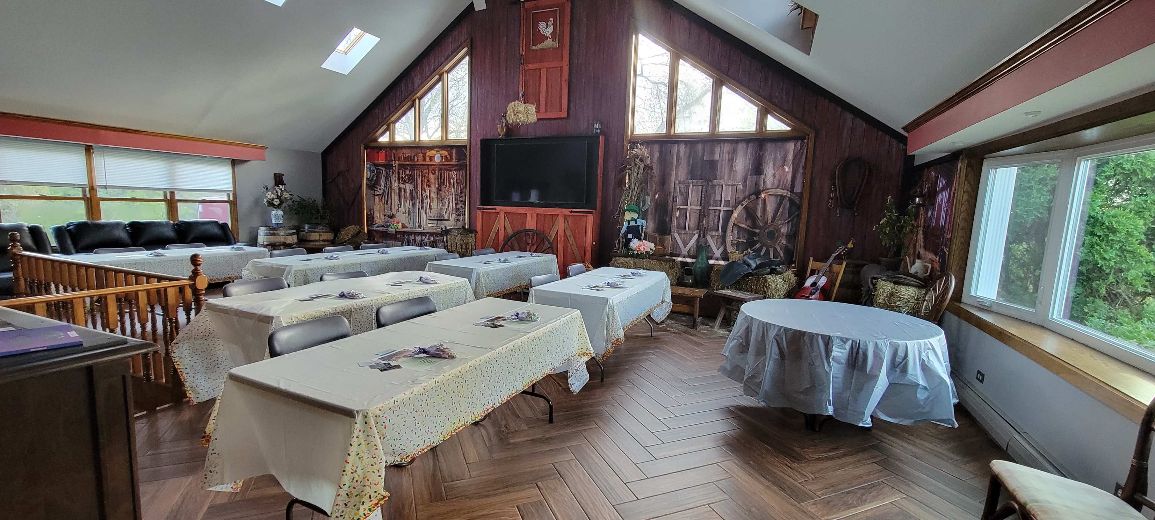 The room features several tables covered with white tablecloths, arranged in a spacious area with a large window and wooden decor.